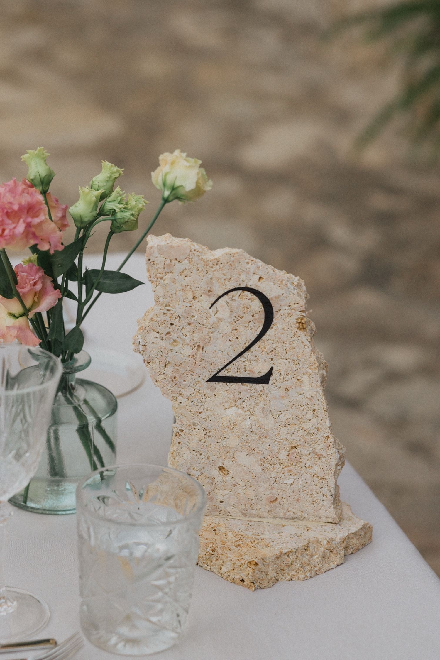 Rustic table numbers made from torn paper with delicate pink and white flowers in glass vases for wedding decor.