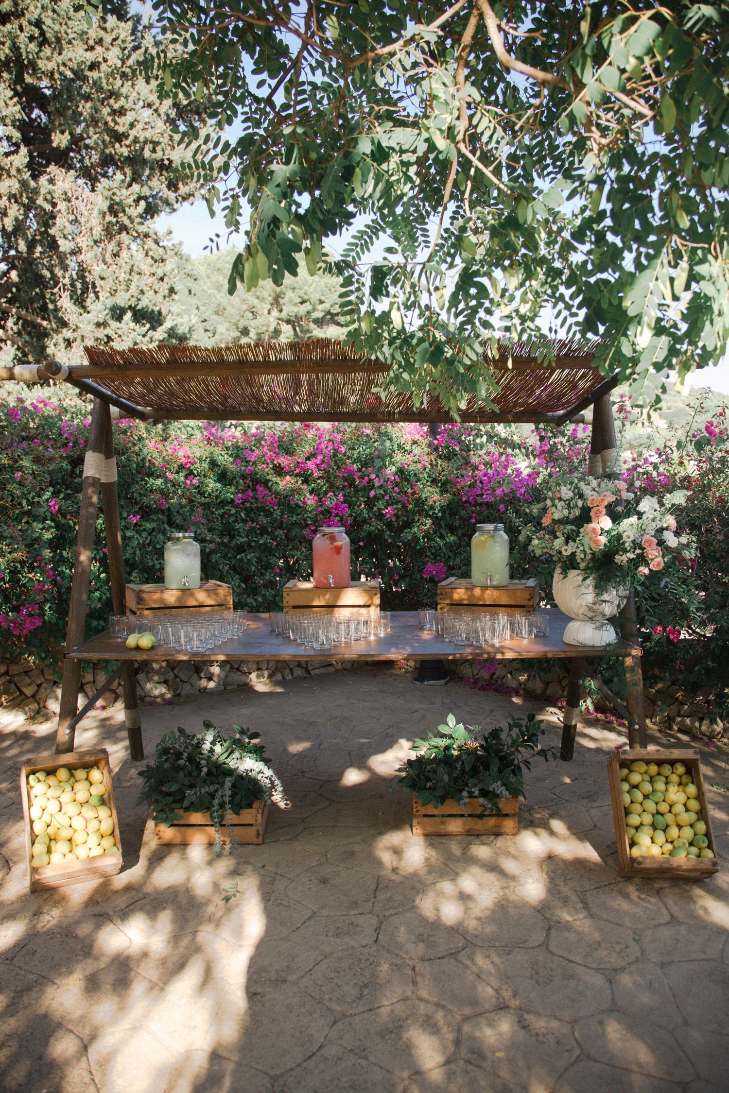Rustic stone bench with colorful bougainvillea flowers climbing along a garden wall in Mediterranean style setting.