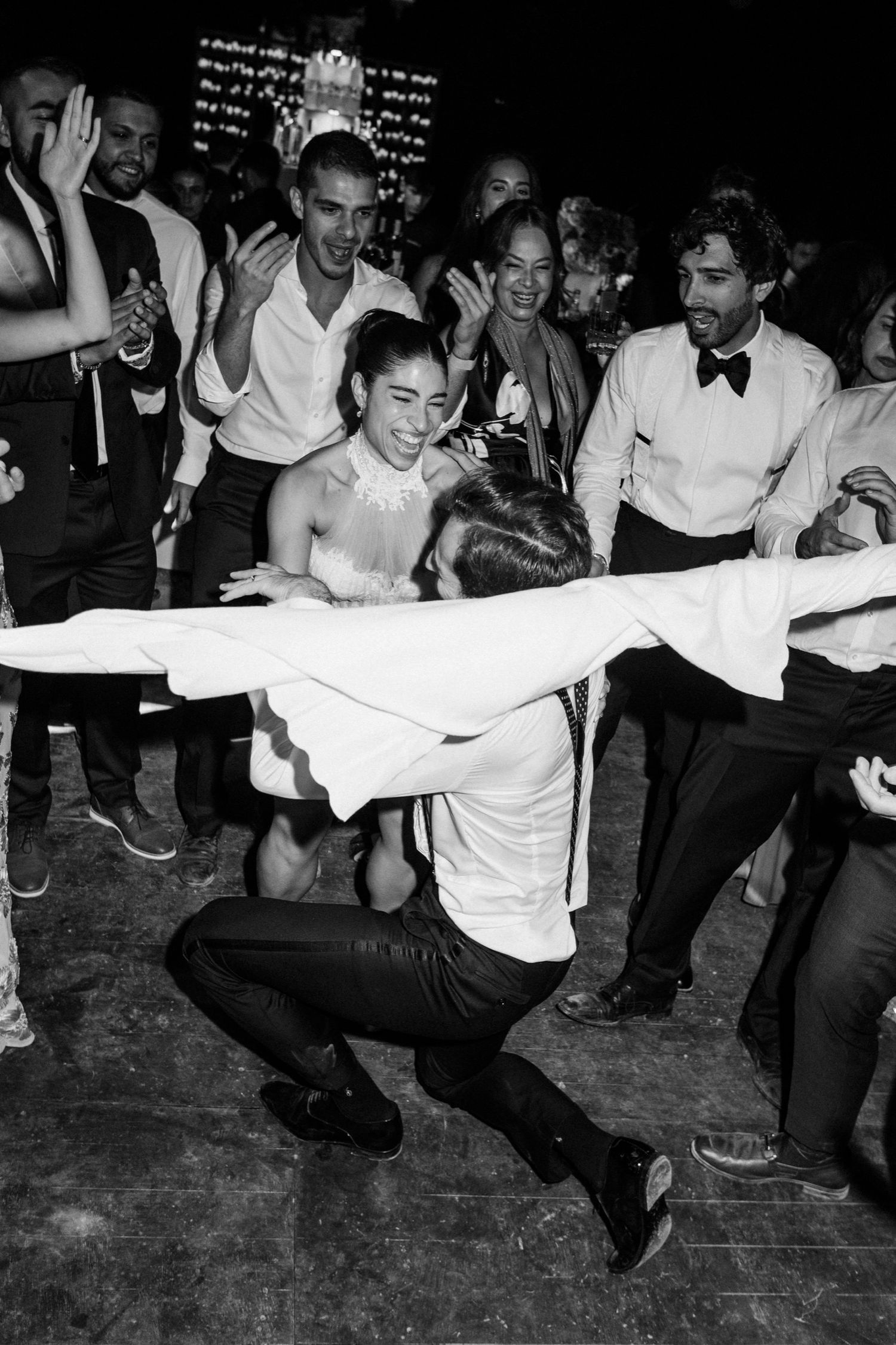 A joyous wedding celebration with guests dancing and having fun at a lively reception party in black and white.