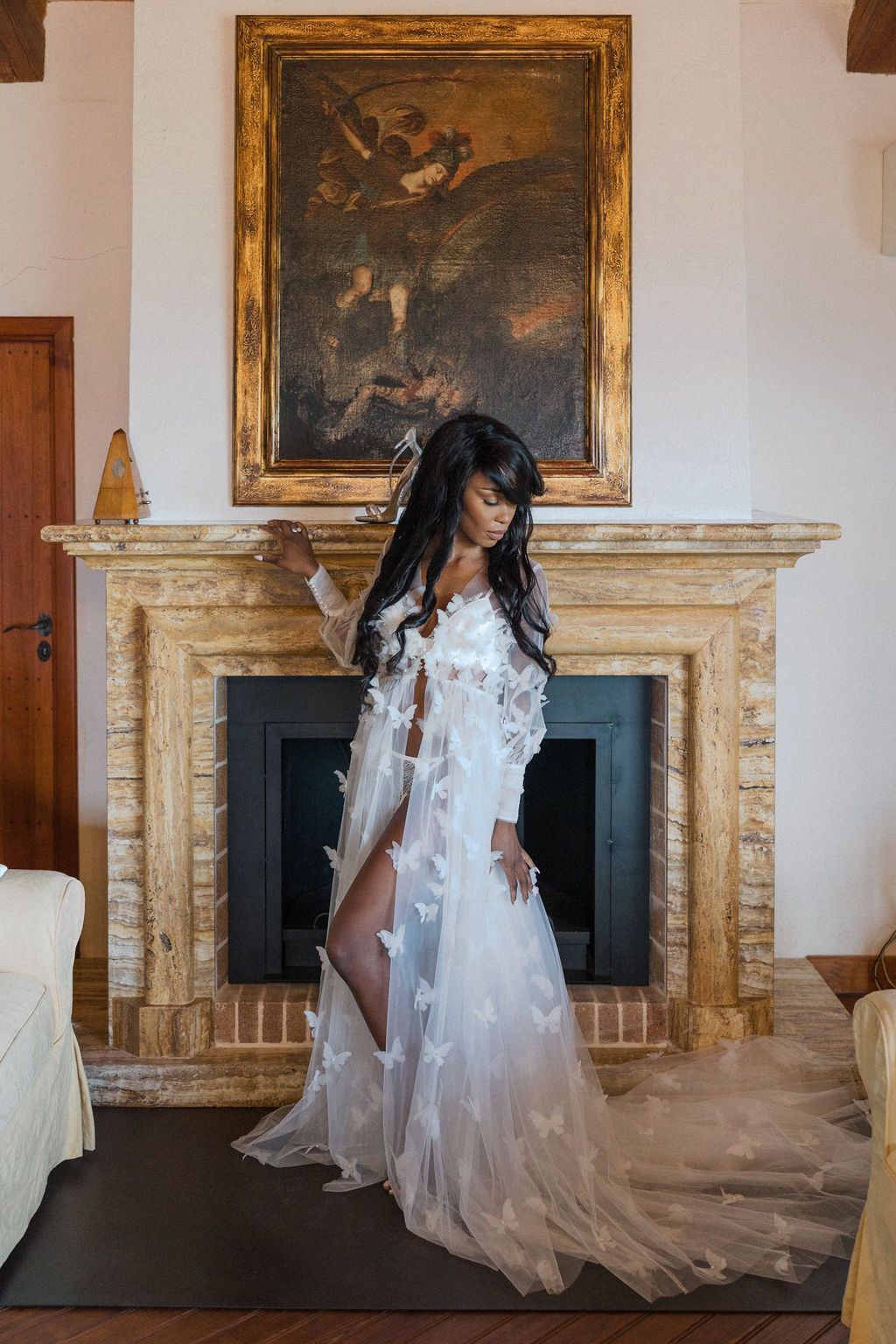 Flowing white bridal robe captured in front of an ornate fireplace with classical artwork.