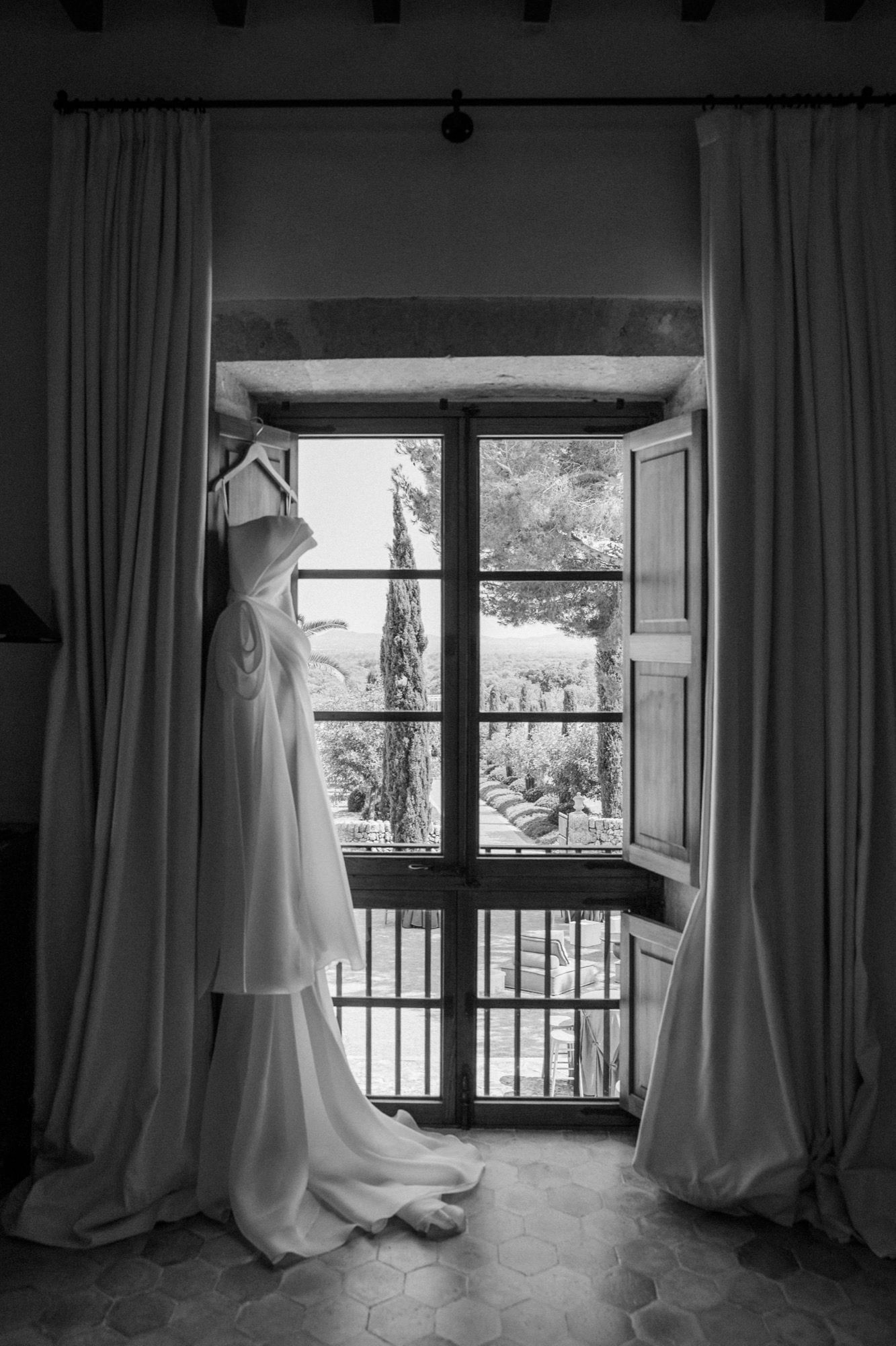 Wedding dress silhouette against window with flowing curtains in dramatic black and white.
