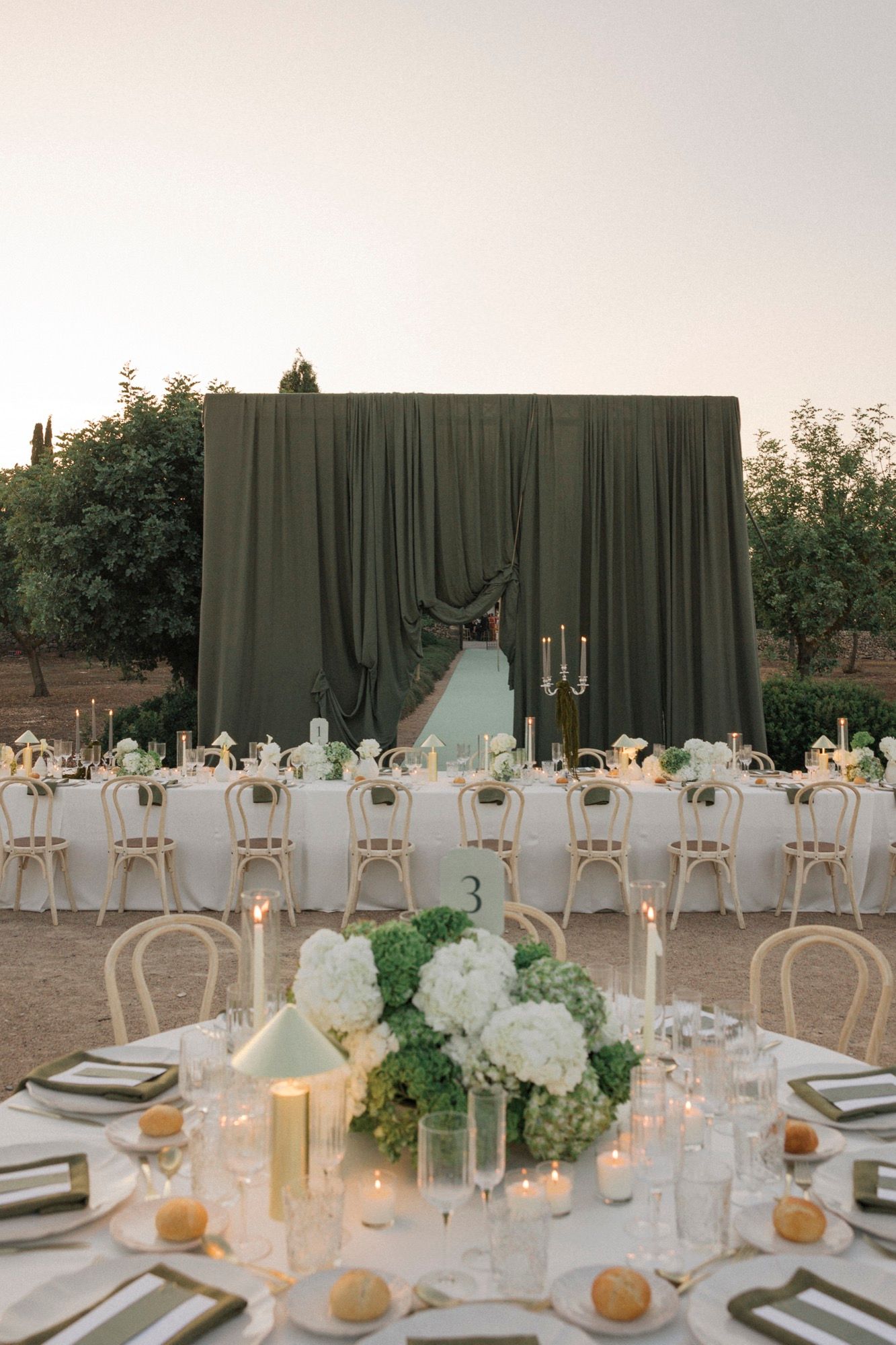 Elegant outdoor wedding reception setup with white chairs and floral centerpieces at sunset.