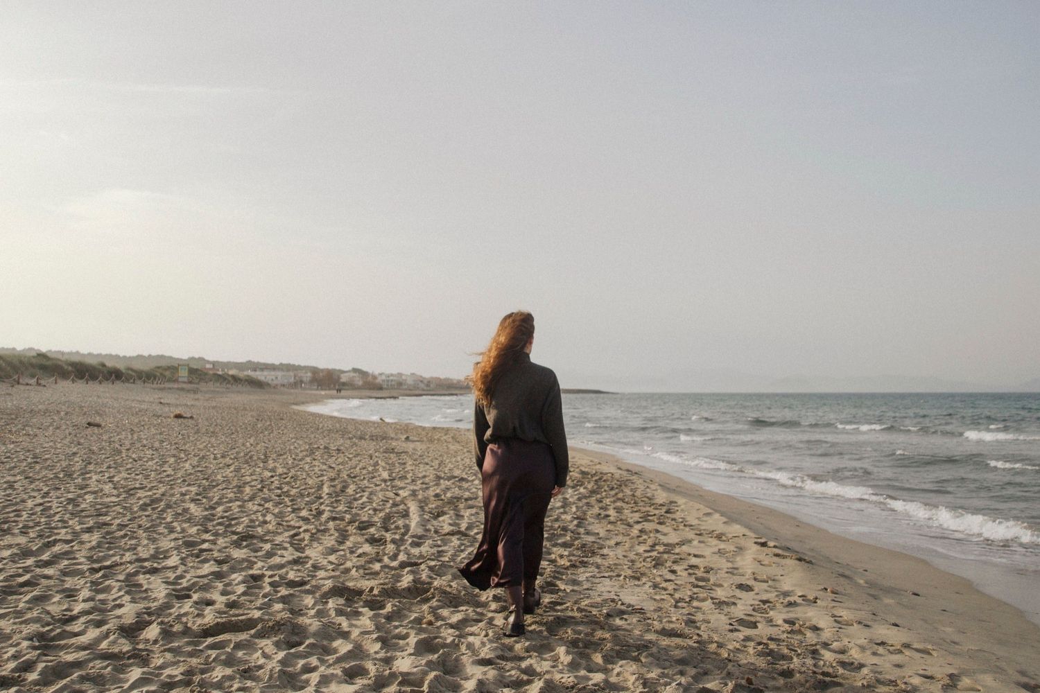 A person walks along a misty beach shoreline at sunset while waves crash against the sand.