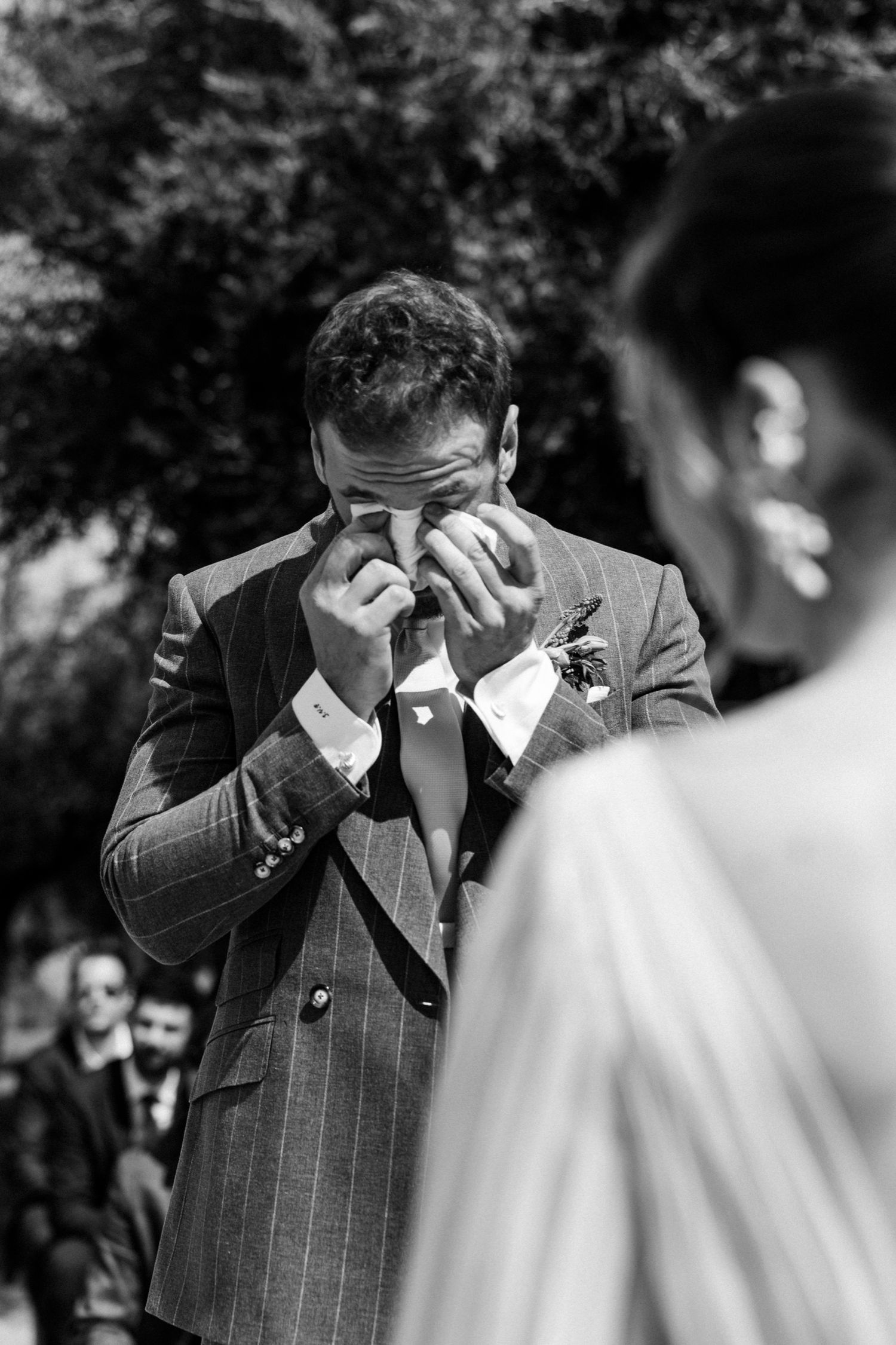 A groom in a pinstriped suit becomes emotional during a wedding ceremony as he sees his bride for the first time.