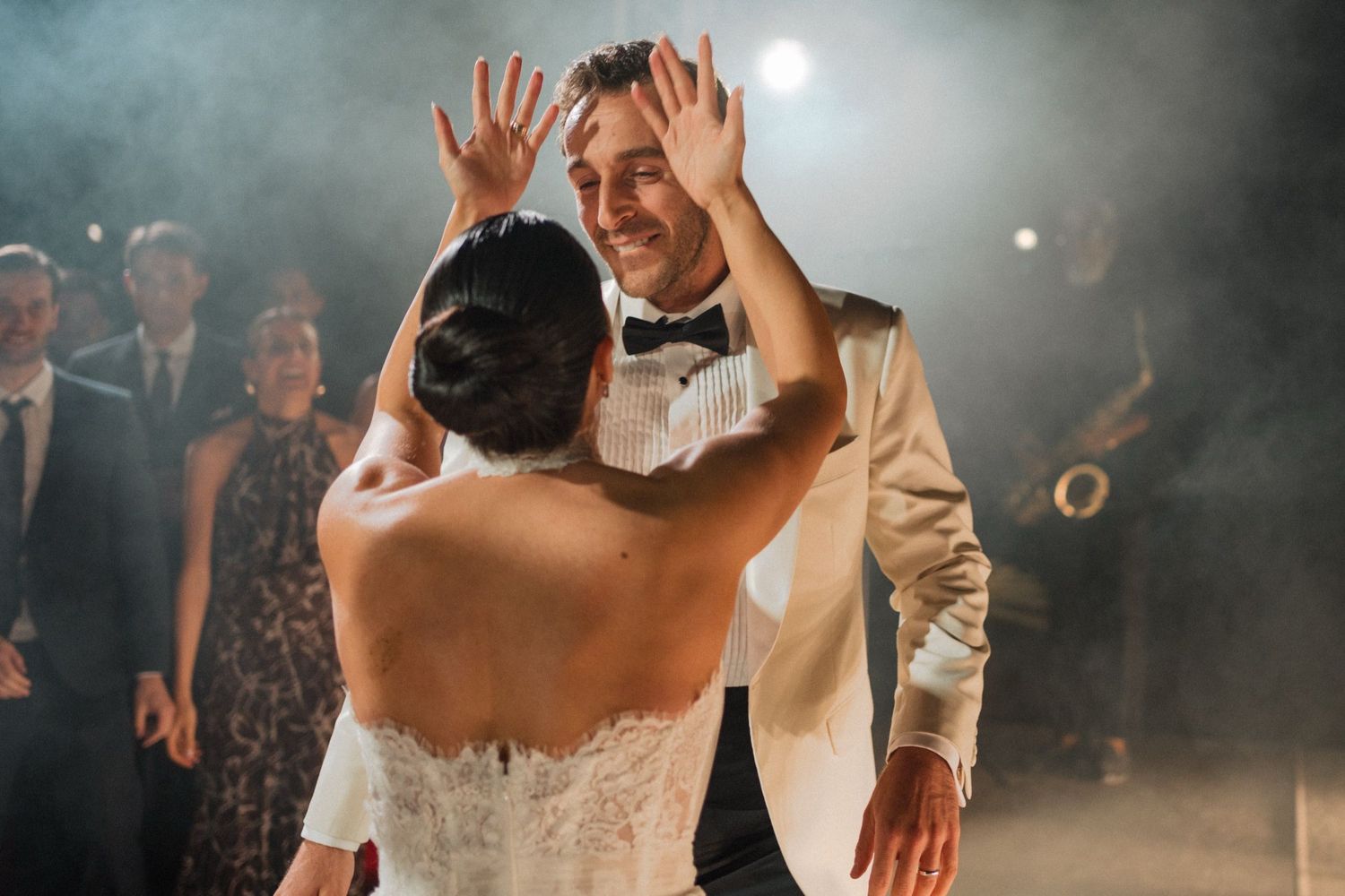 Wedding couple dances together at their reception while guests watch and celebrate in a dimly lit venue.