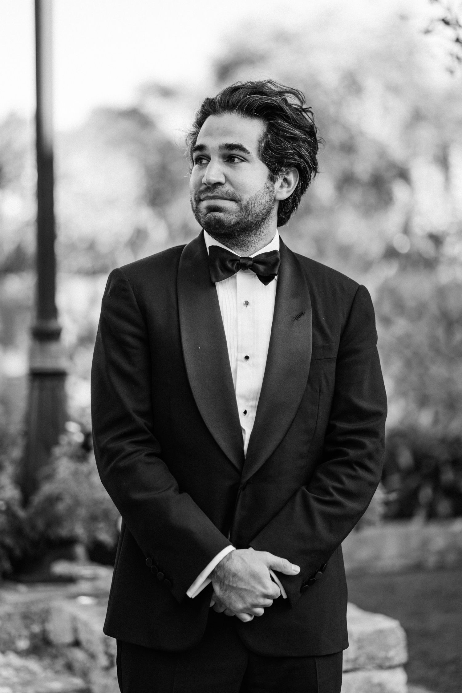 A black and white collage of a man in a tuxedo posing in four different elegant poses outdoors.