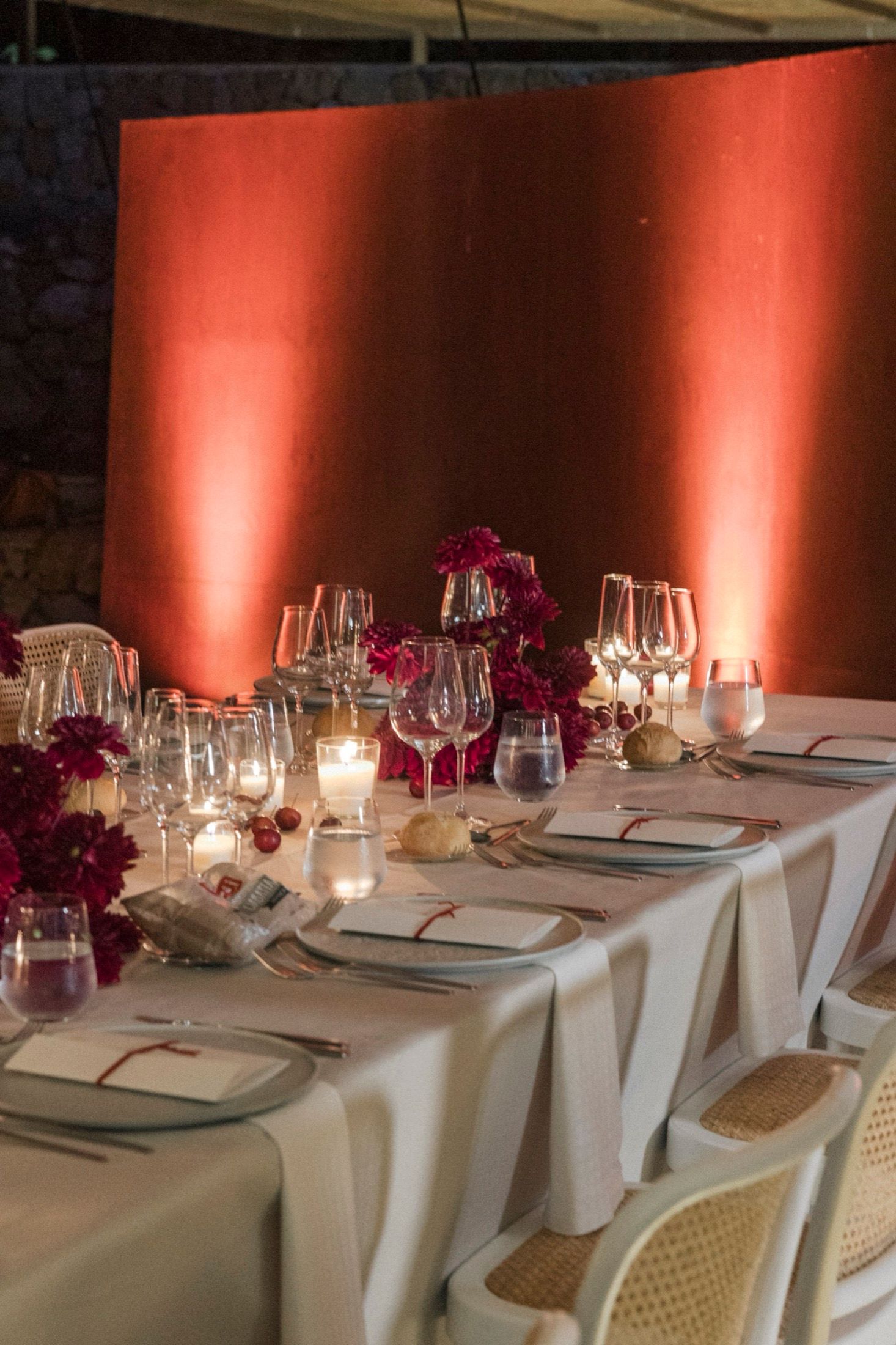 Elegant wedding table setting with white linens, crystal glassware, candlelight and deep magenta floral centerpieces.