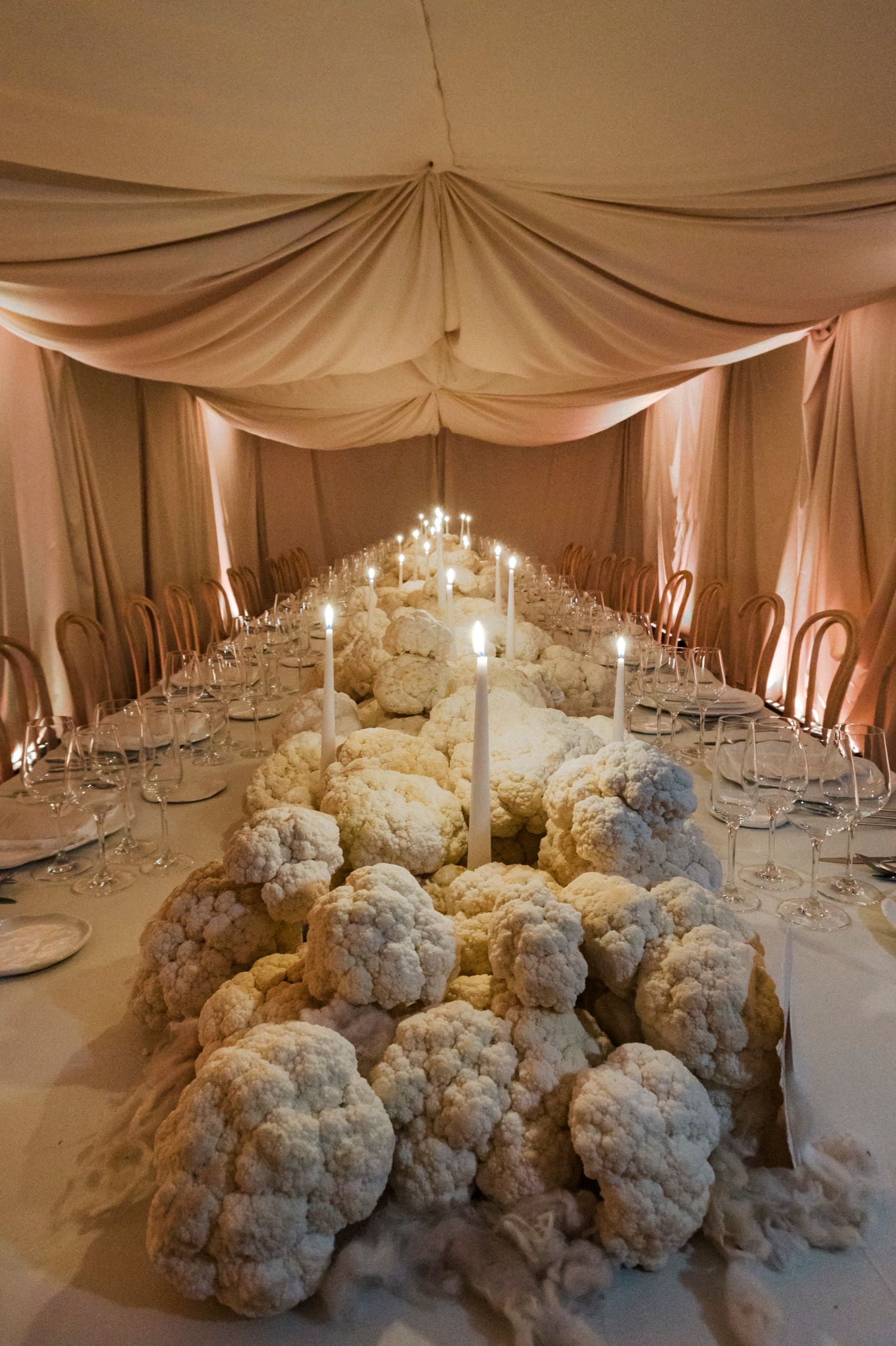 Luxurious wedding table setting with dramatic white floral centerpieces and draped fabric ceiling.