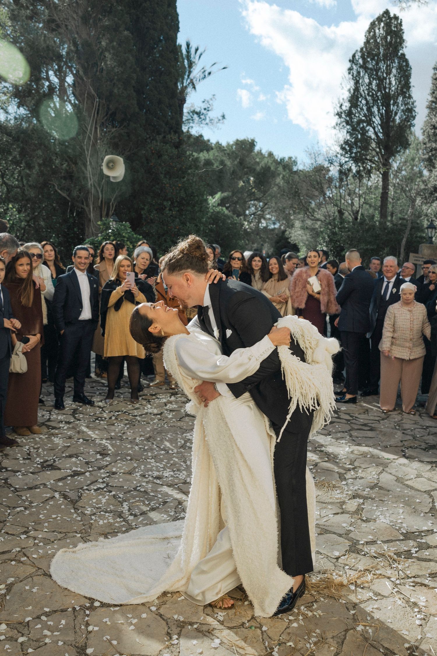 Wedding celebration with dancing couples in formal attire on stone courtyard.