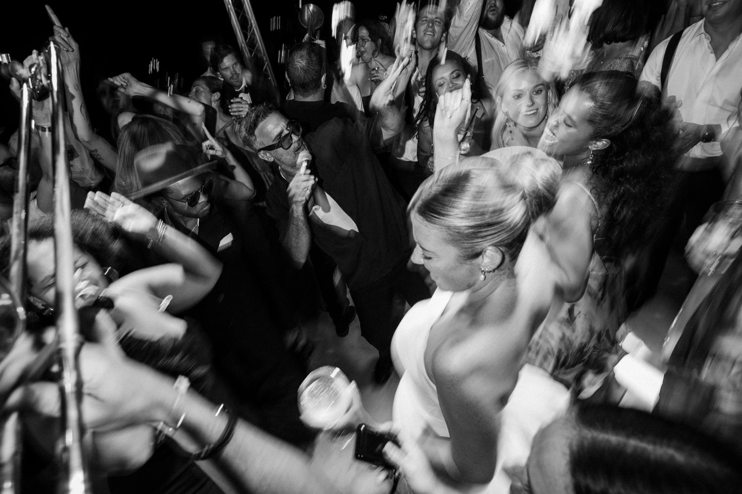 Black and white photo captures energetic dancing and celebration at wedding reception.