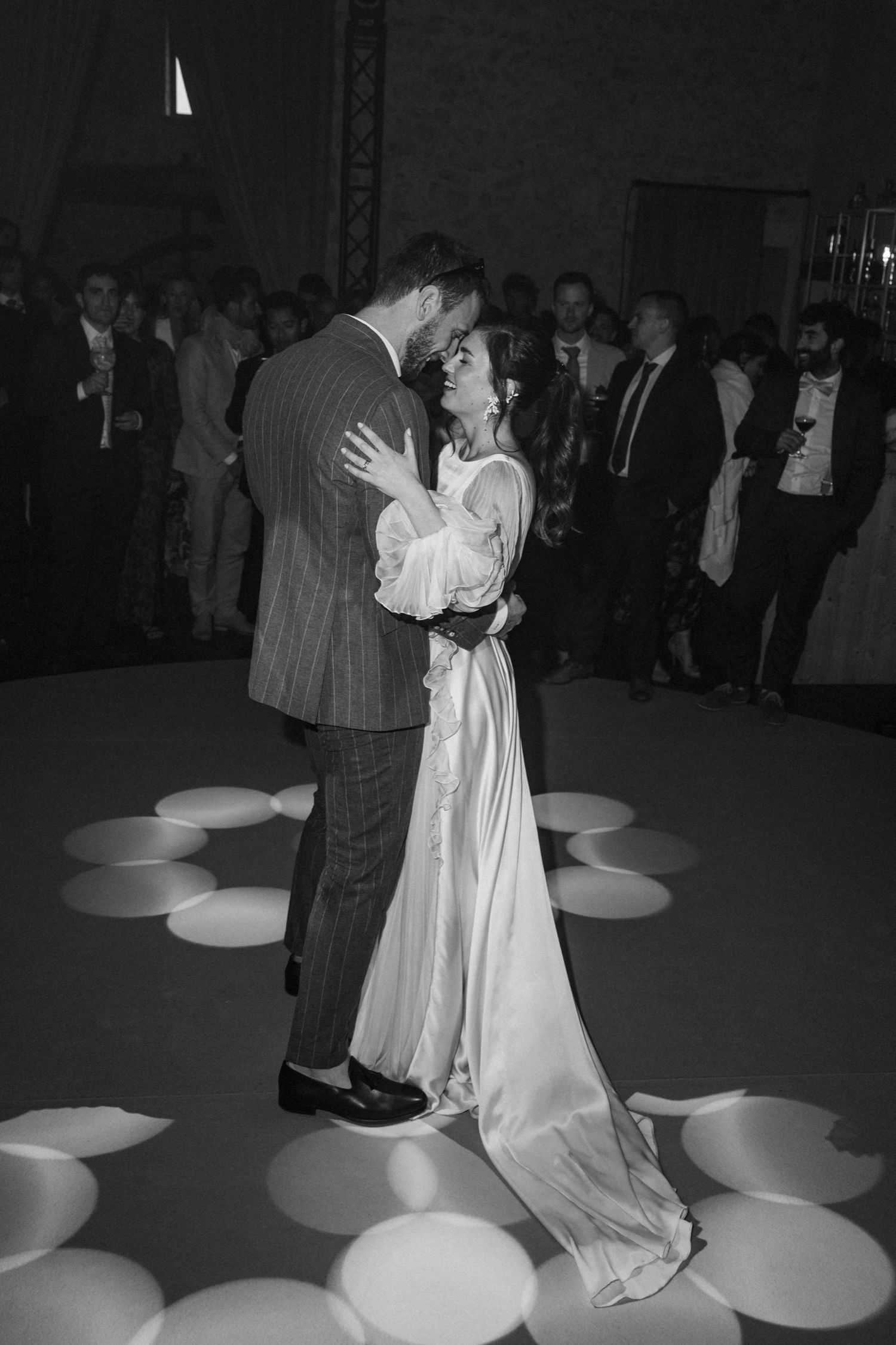 A couple shares a romantic dance on a spotlit dance floor with circular light patterns during what appears to be a wedding reception.