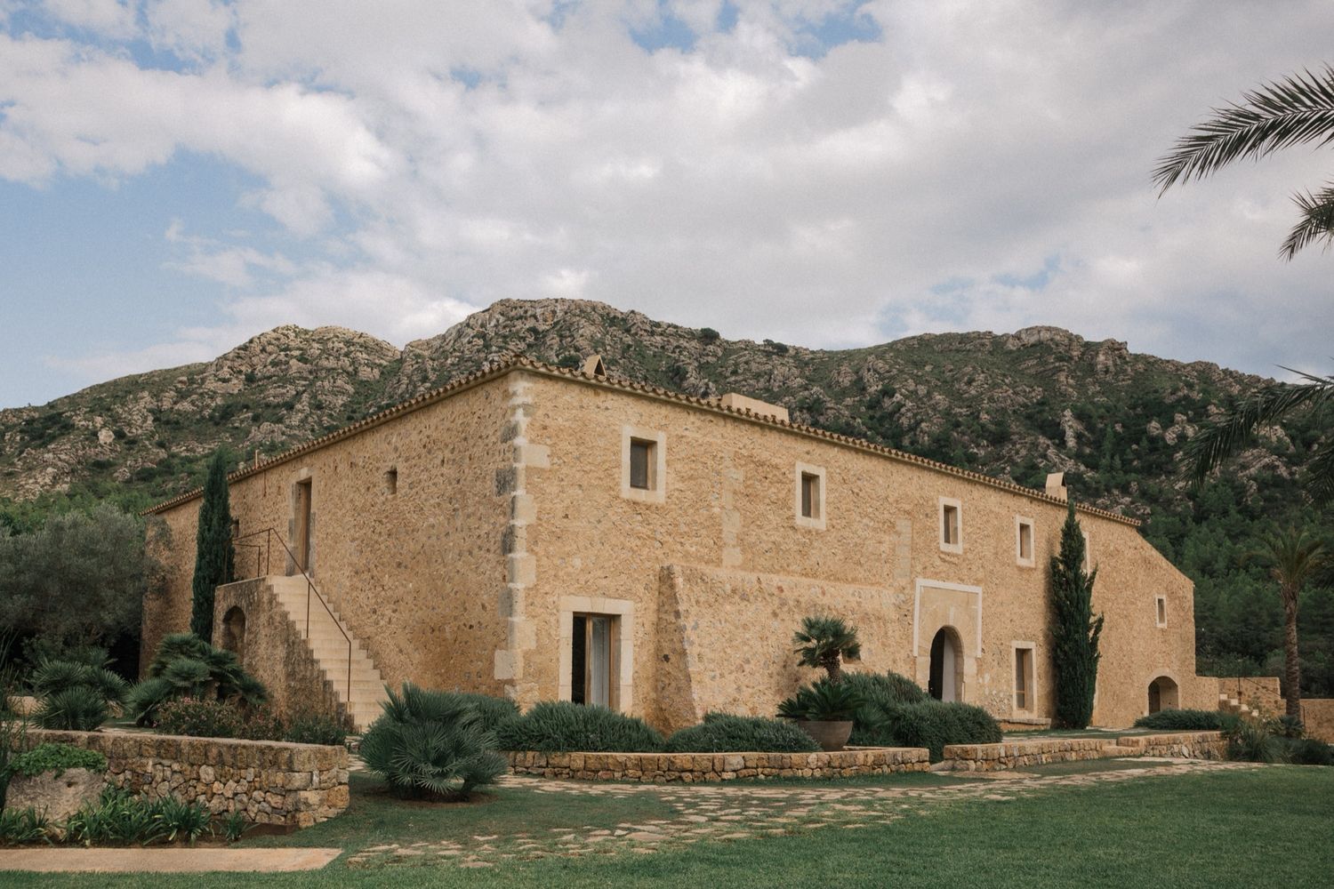 A panoramic view of historic stone buildings nestled against a mountainous landscape in warm sunlight.
