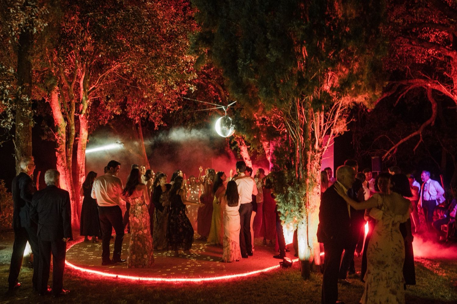A nighttime forest path illuminated with red lights creating a magical glowing atmosphere through the trees.