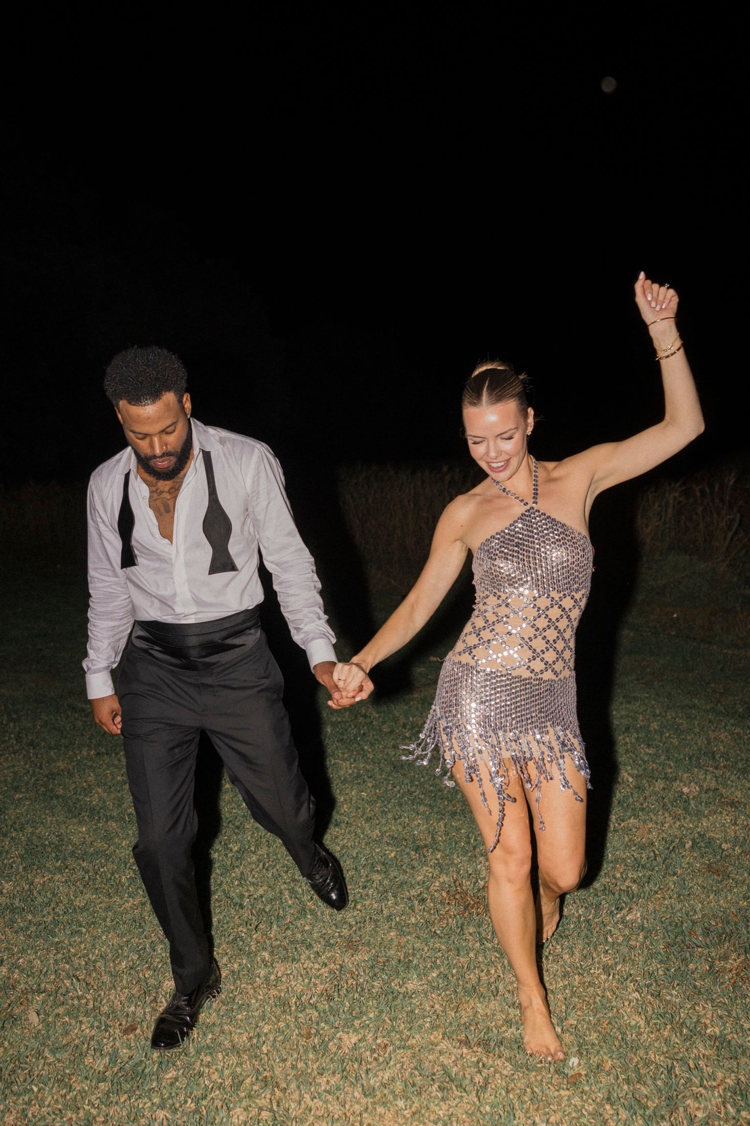 A joyful couple dancing barefoot on grass at night.