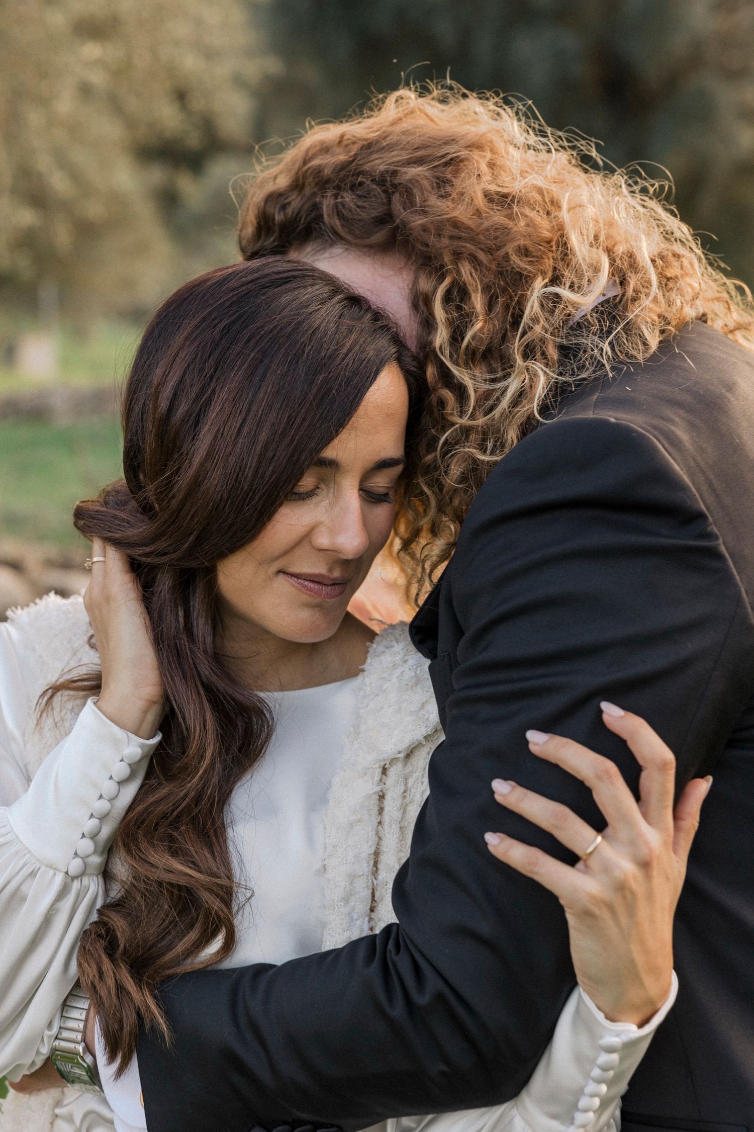 An intimate close-up portrait capturing a tender embrace against a natural outdoor setting.