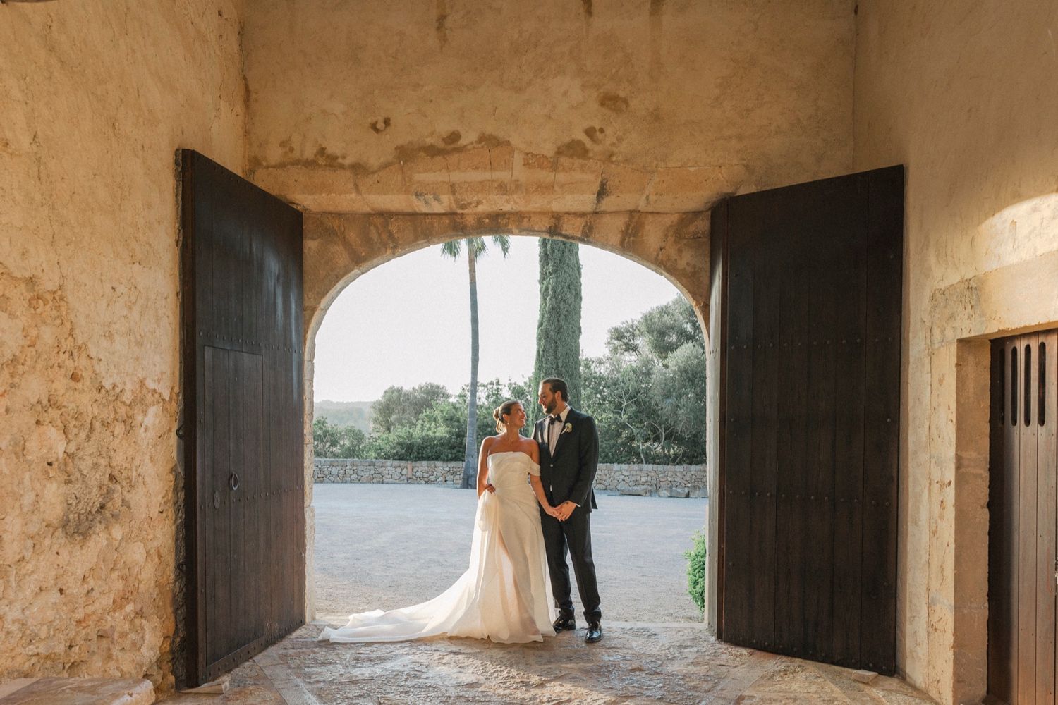 Stone tunnel with rustic wooden doors creates dramatic wedding photo setting.