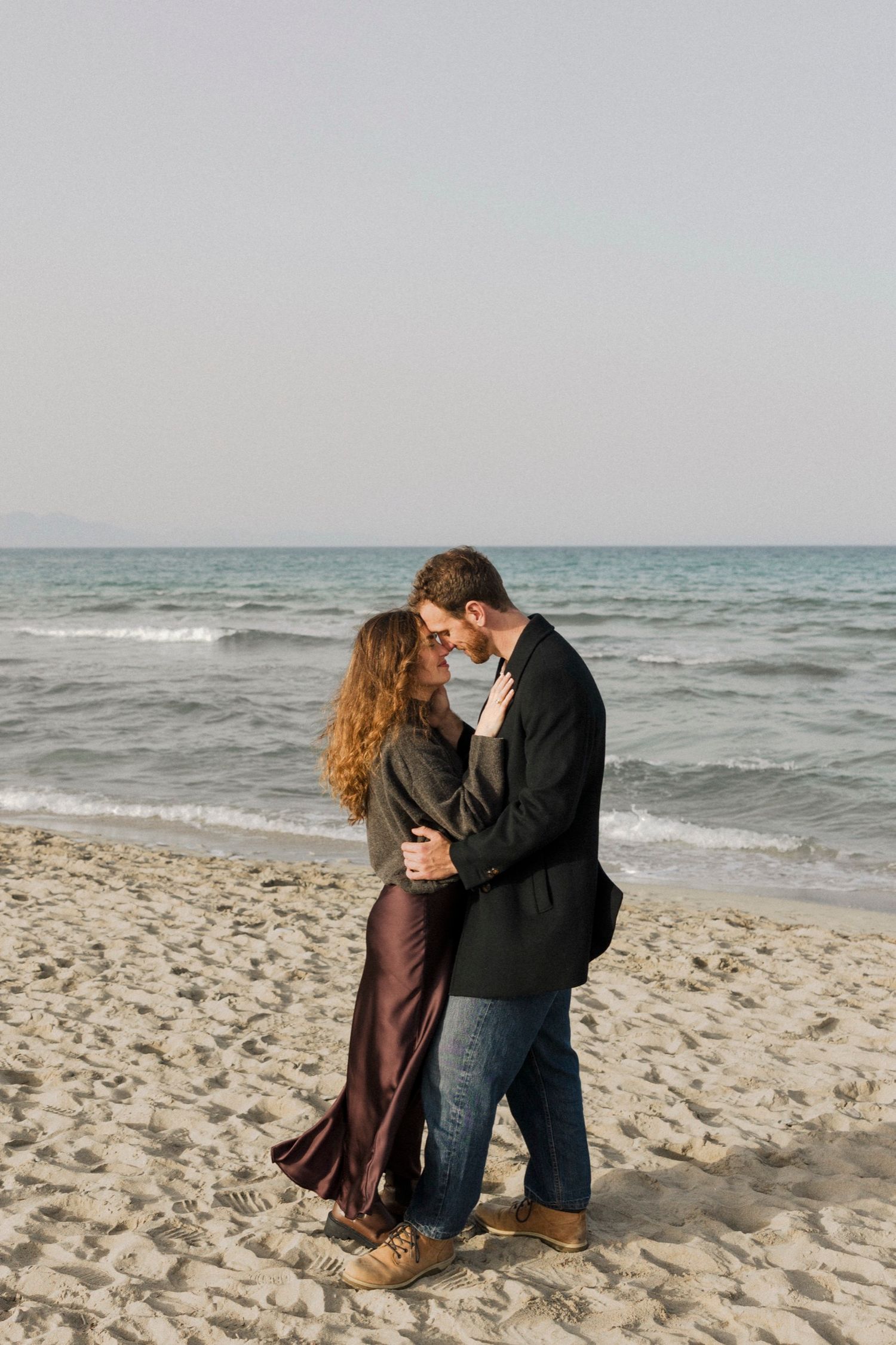 Couple sharing intimate moments together on a sandy beach with waves in the background.