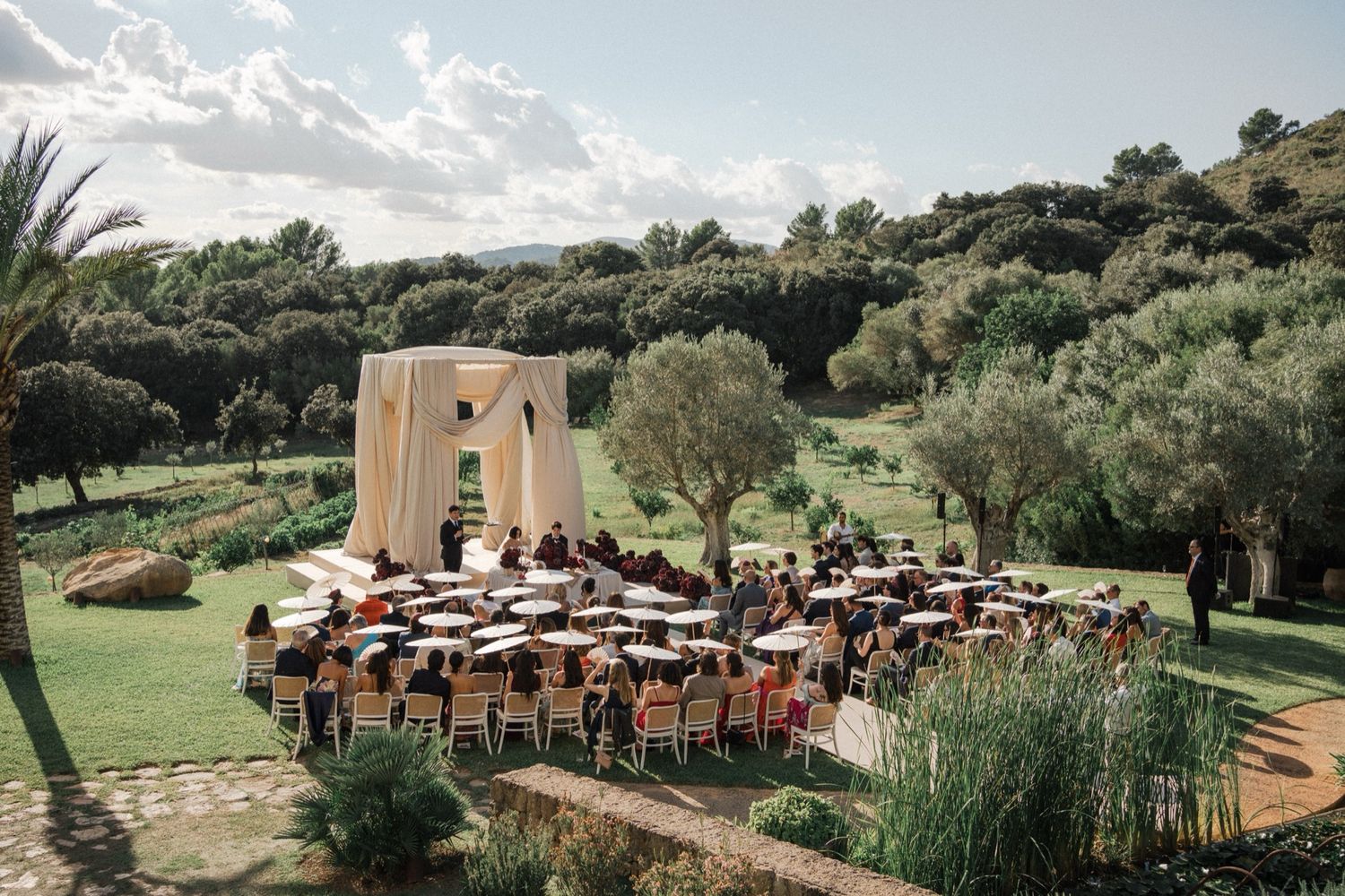 Panoramic view of an outdoor wedding reception setup with rustic tables and chairs surrounded by lush greenery.