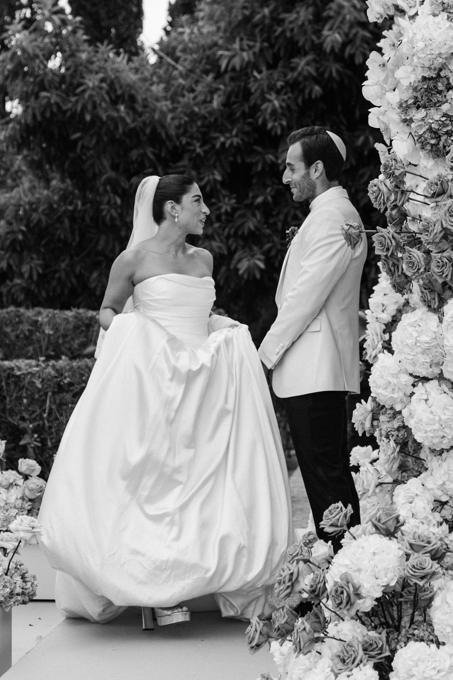 Black and white wedding photo series showing bride and groom dancing together among elegant white floral decorations.