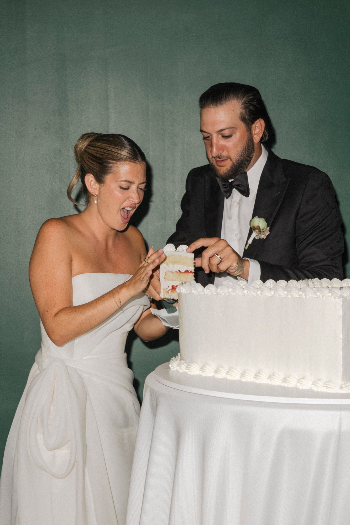 Couple playfully takes bites of wedding cake together at their reception.
