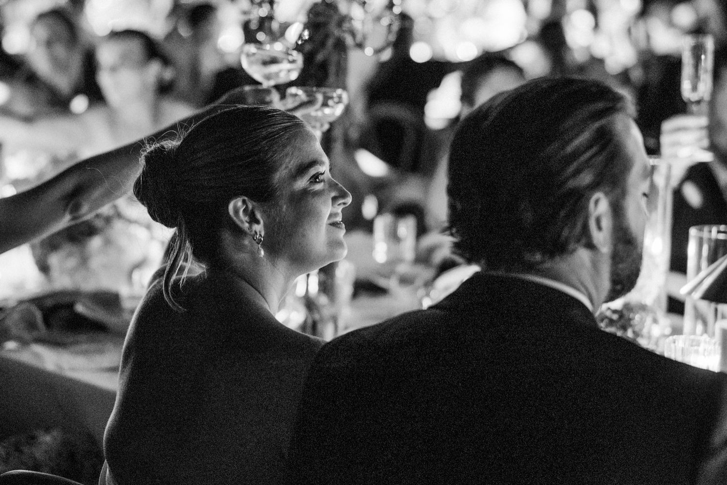 Black and white candid shot of wedding guests seated at an elegant dinner reception.
