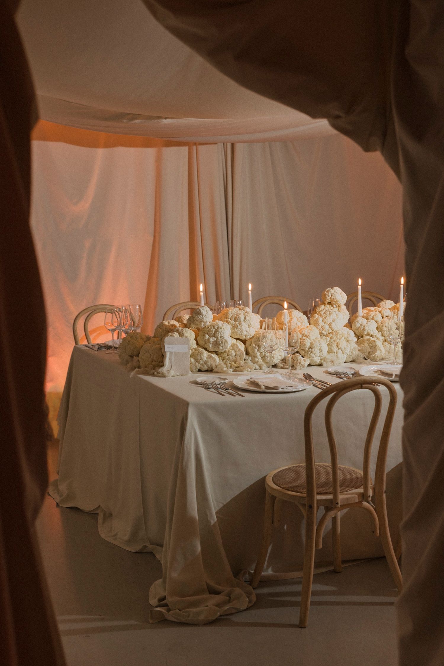 Elegant wedding reception tables set with white linens and floral centerpieces under draped fabric ceiling.