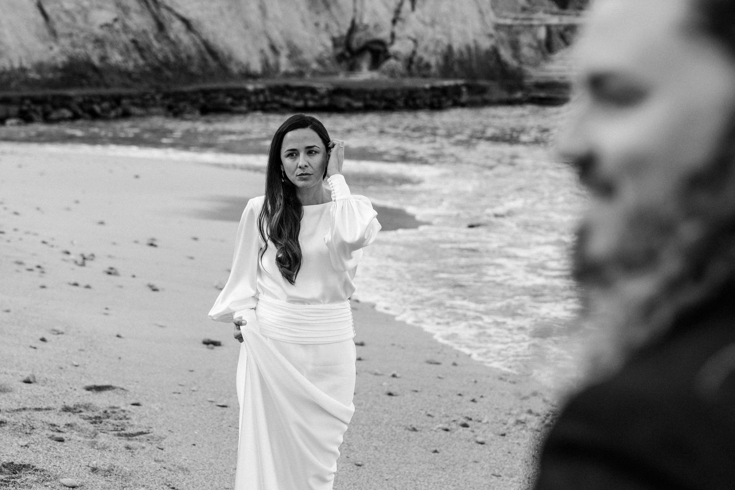 Black and white photograph of figures walking along a rugged beach with cliffs.