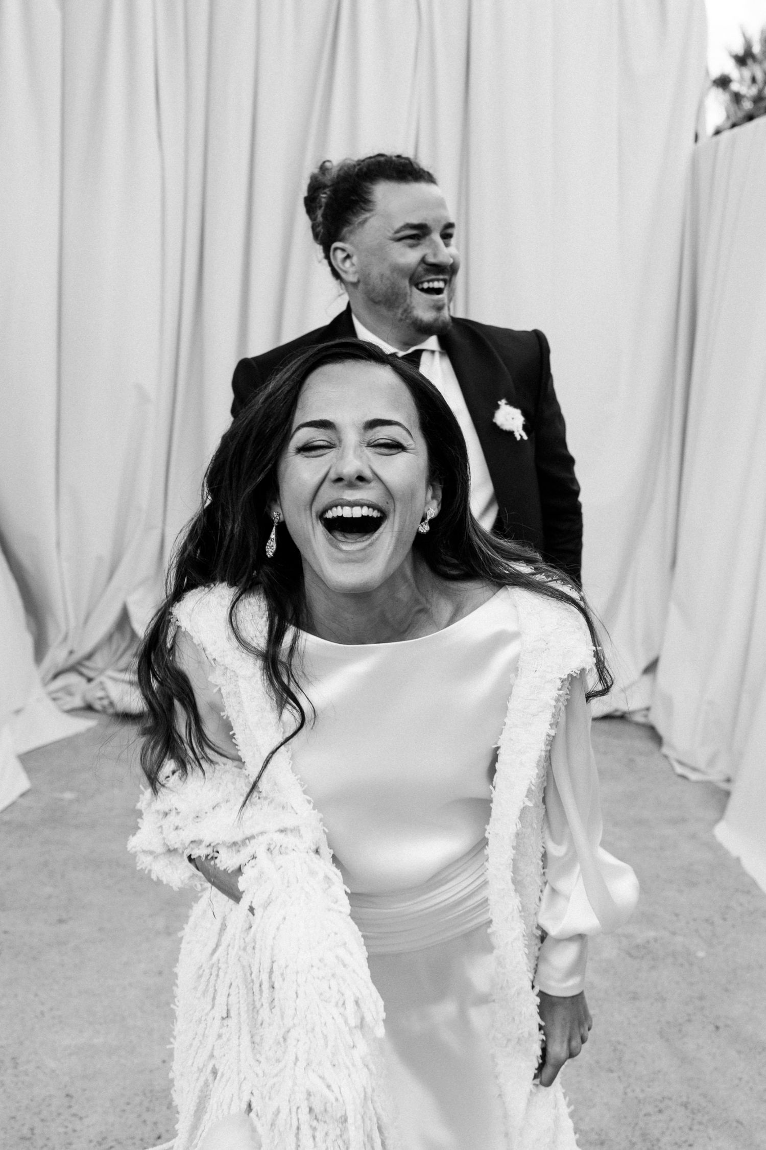 A bride in a white dress laughs joyfully during a candid wedding moment.