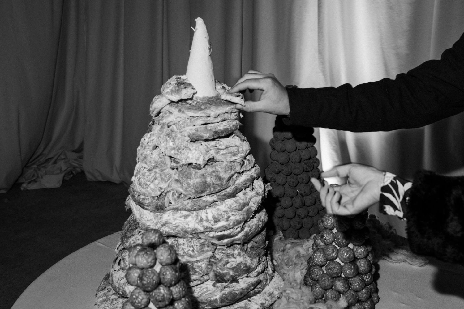 Hands placing decorative elements on a tiered wedding dessert display.