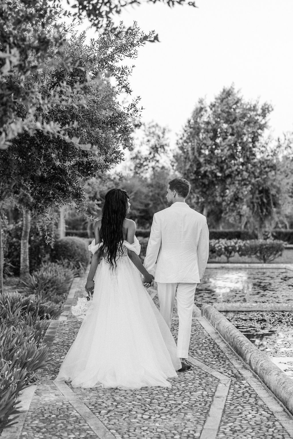 Wedding couple walking along stone pathway in garden setting.