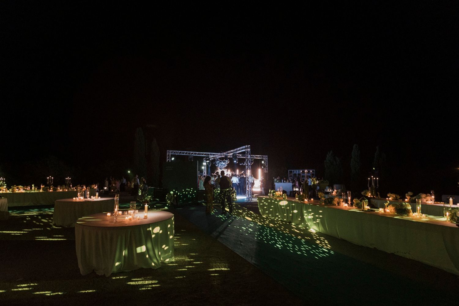 Outdoor wedding reception venue illuminated by candlelight and string lights at night.