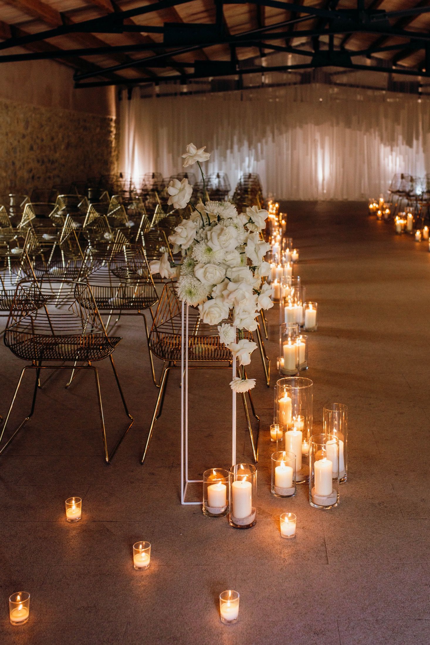 Candlelit wedding venue setup with wire chairs and glowing lanterns creating a romantic ambiance in an industrial space.