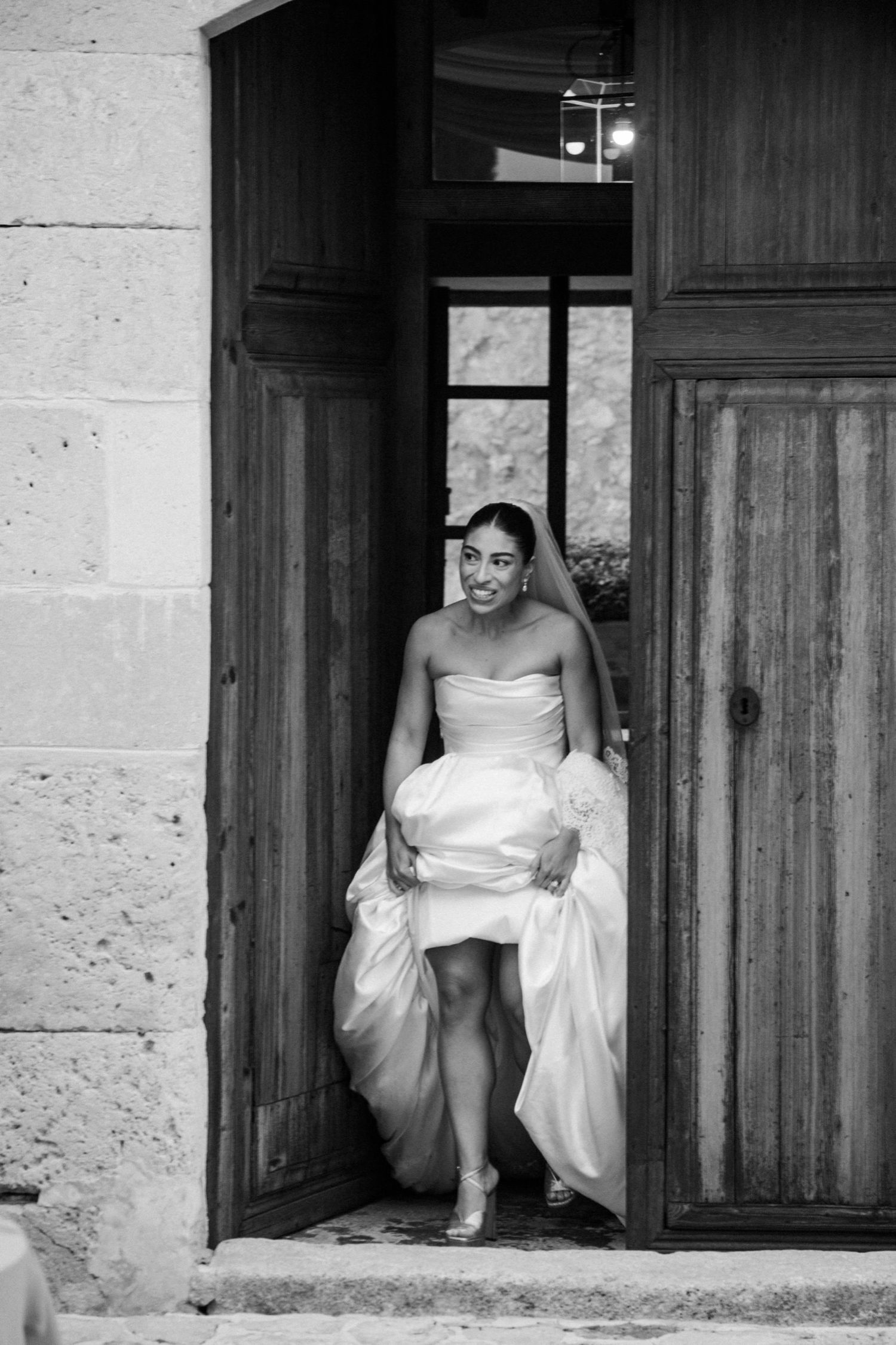 A black and white triptych shows a person in a white dress sitting in doorways of a rustic stone building.