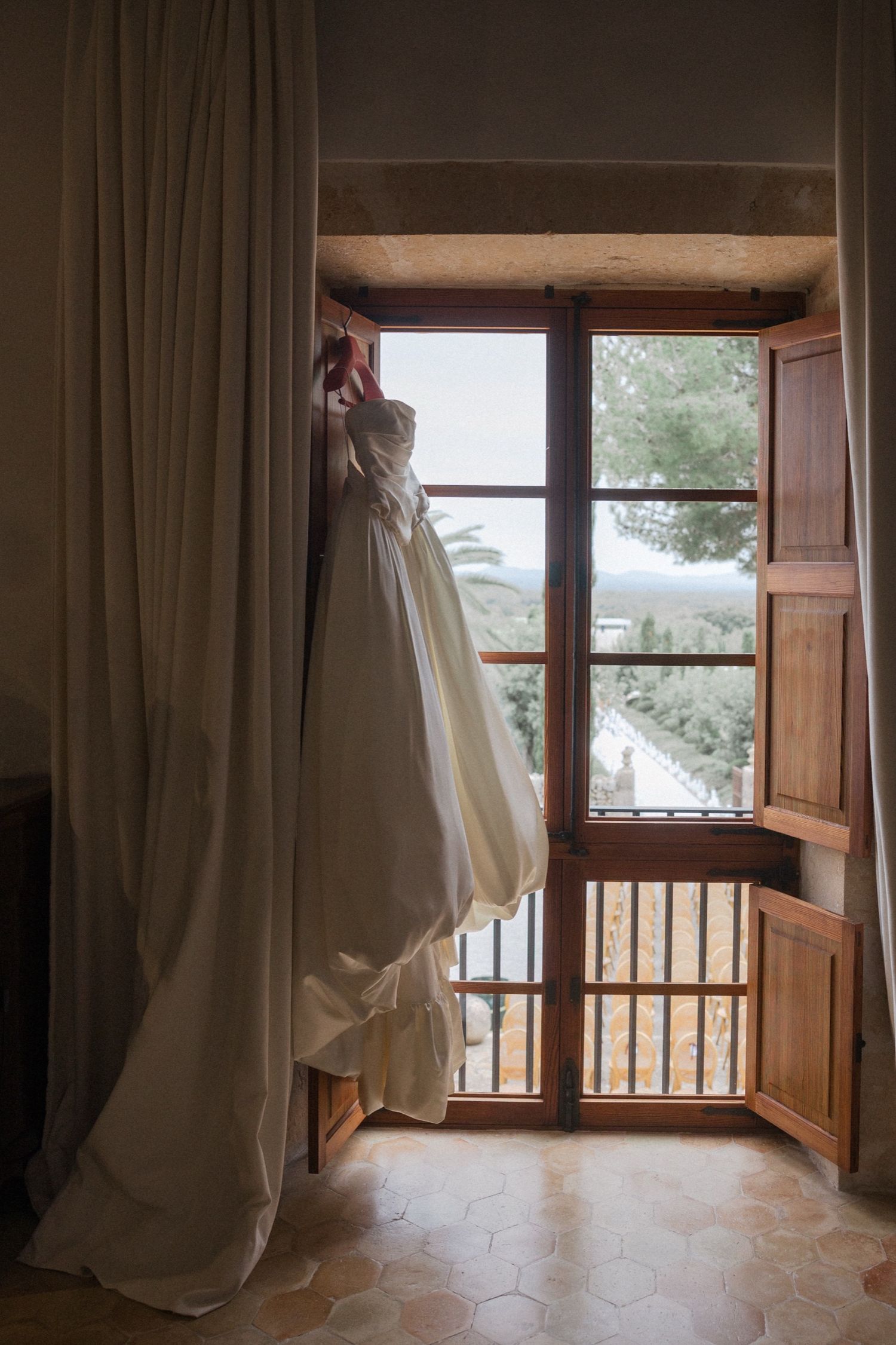 White curtains billow in the breeze through an open wooden window overlooking a scenic mountain landscape.