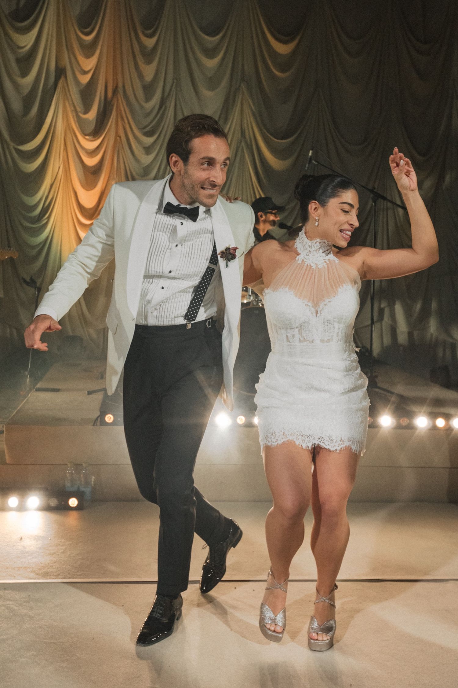 A couple performs a synchronized dance move at their wedding reception on an illuminated dance floor.