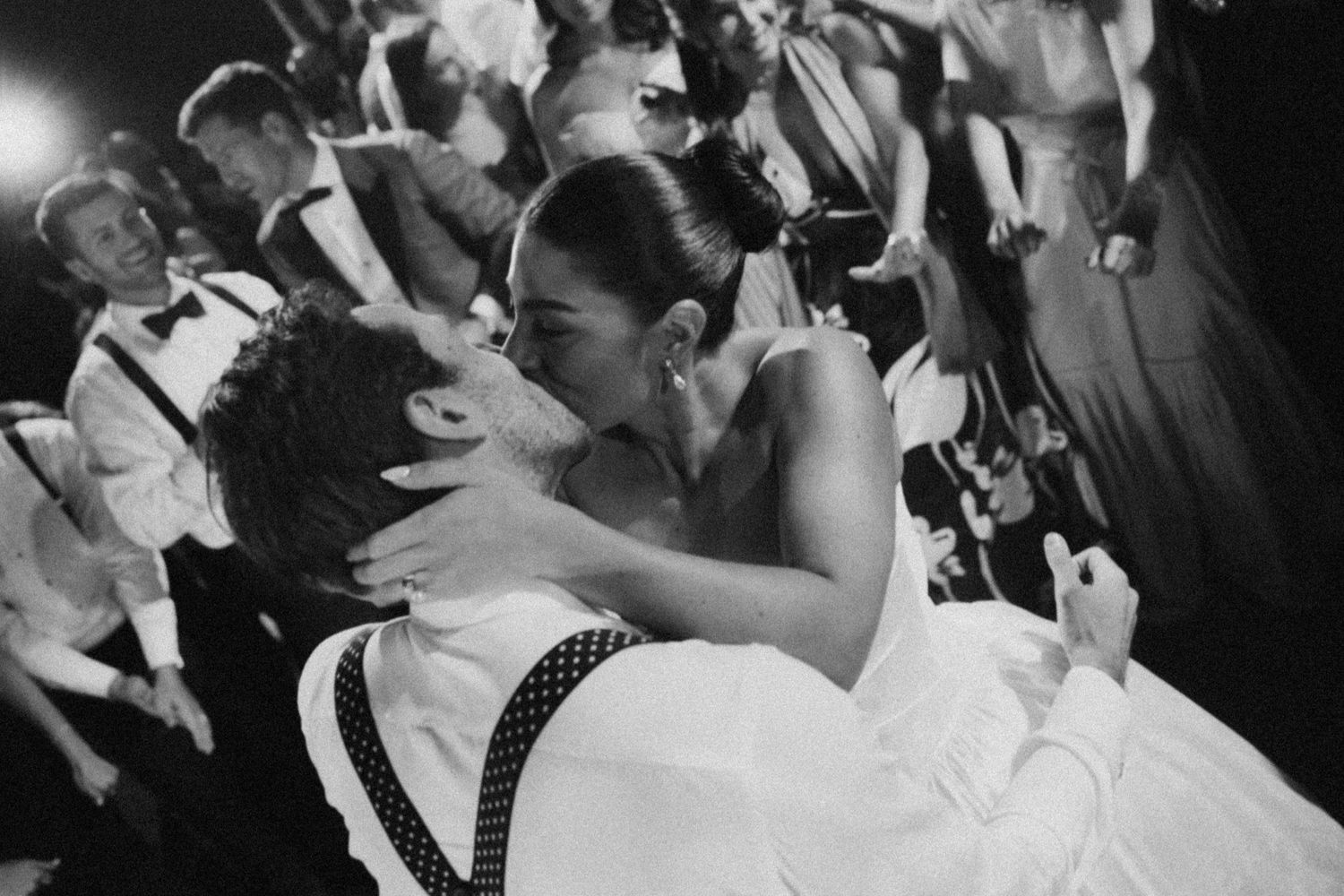 A couple shares a romantic dip and kiss on the dance floor during a wedding celebration in black and white photography.