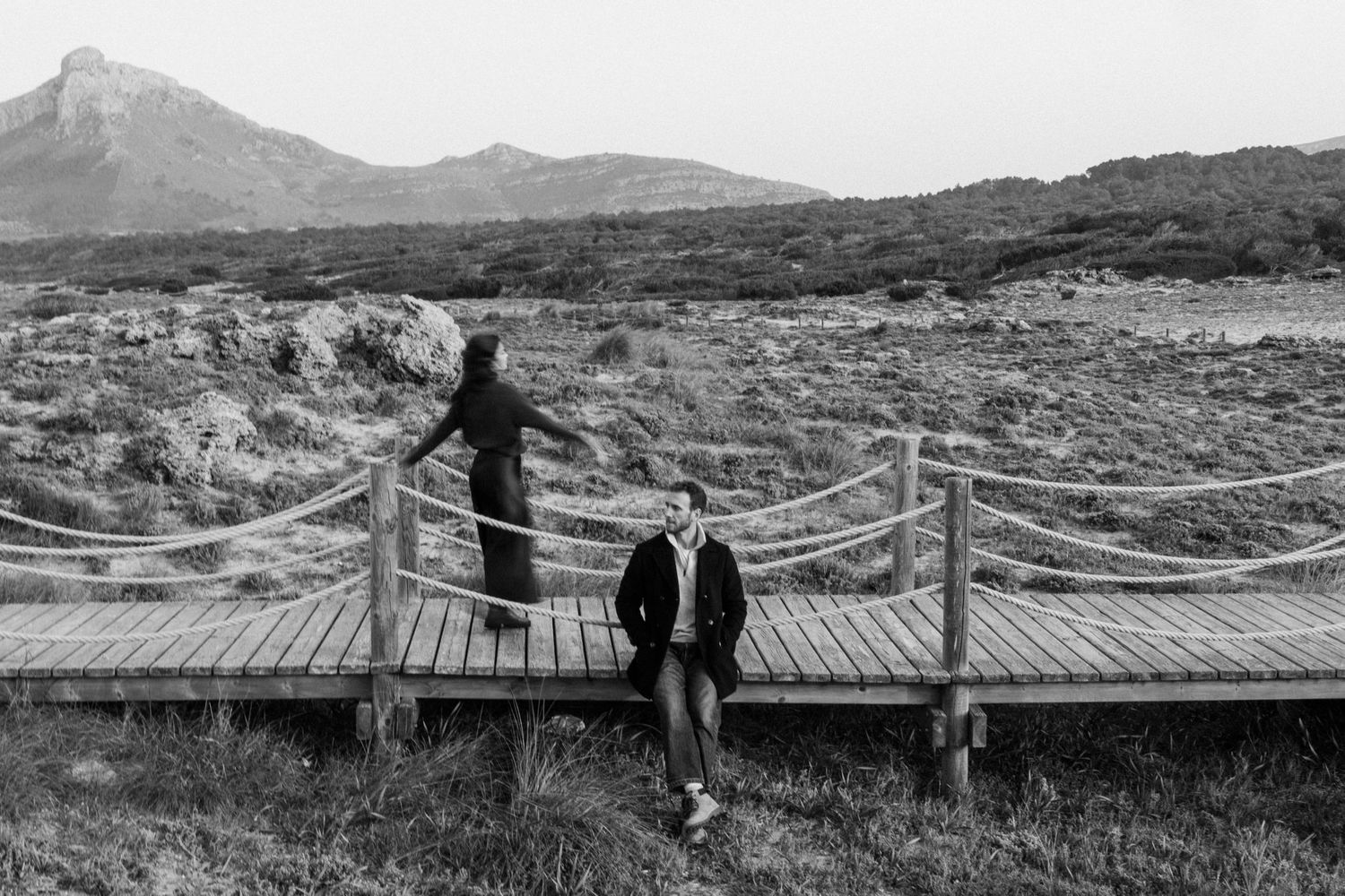 A series of black and white landscape photographs showing people walking on wooden bridges in mountainous terrain.