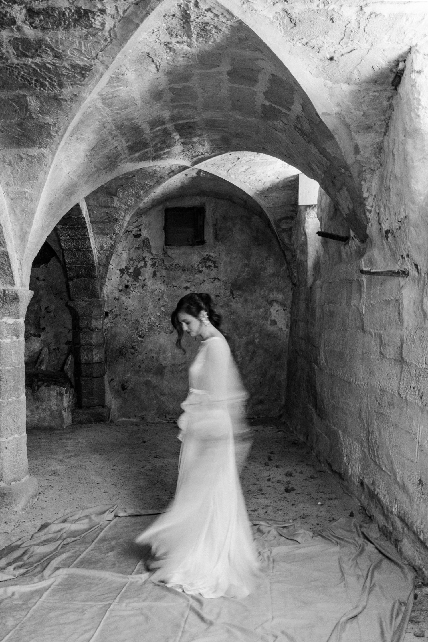 A sequence of black and white photos showing a figure in a white dress moving through a stone archway tunnel.