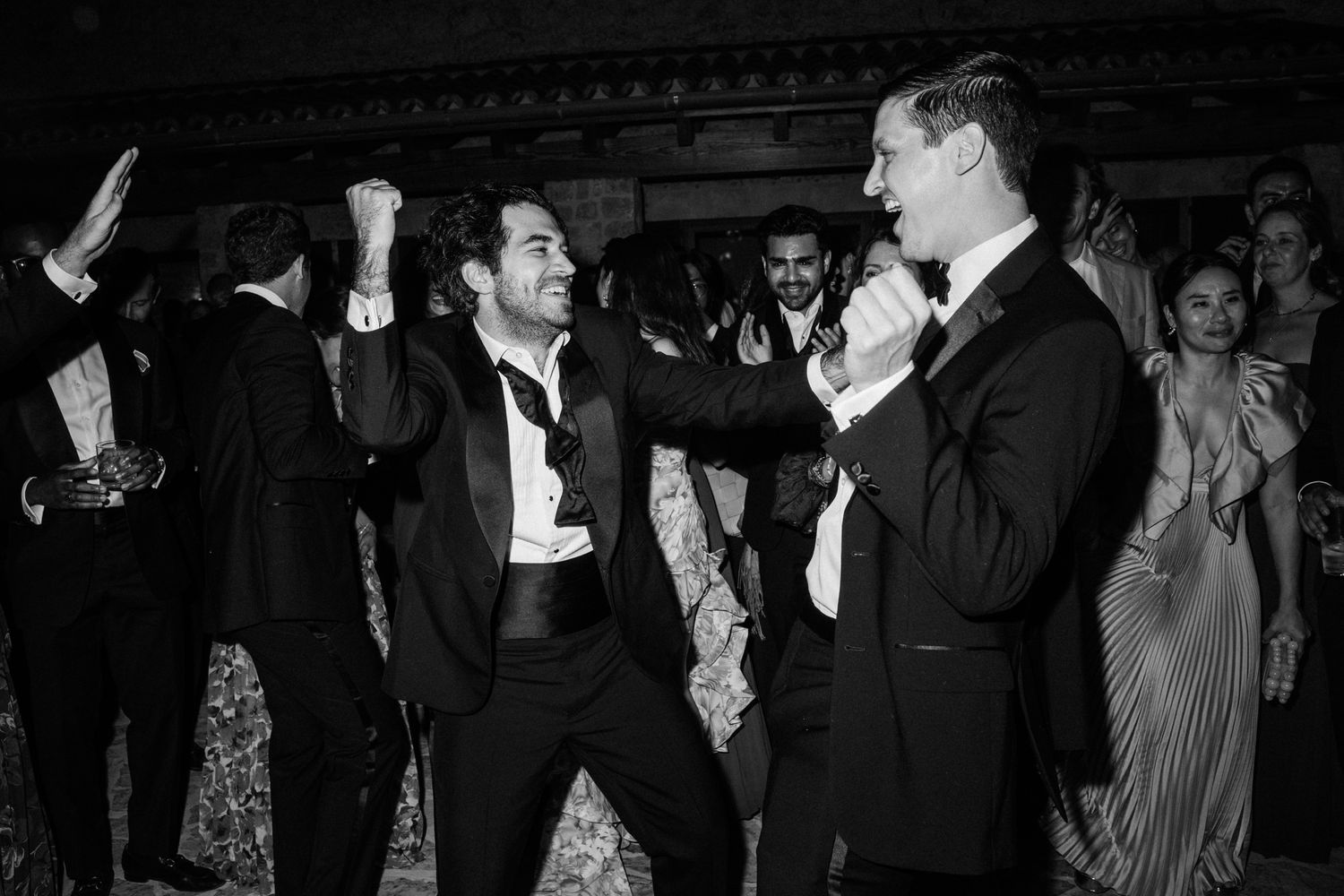 People dancing together in formal attire at what appears to be a wedding reception or celebration in black and white.