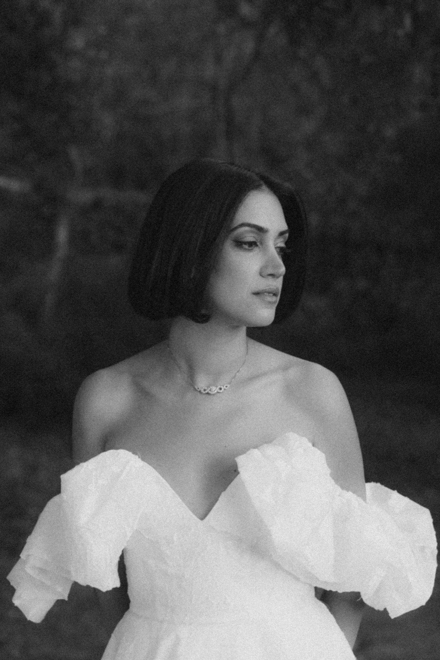 Black and white portrait of a woman in an elegant white off-shoulder dress with a delicate necklace.