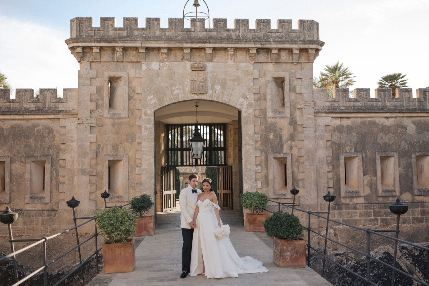 Bride and groom posing in front of a grand stone castle gate during their wedding day.