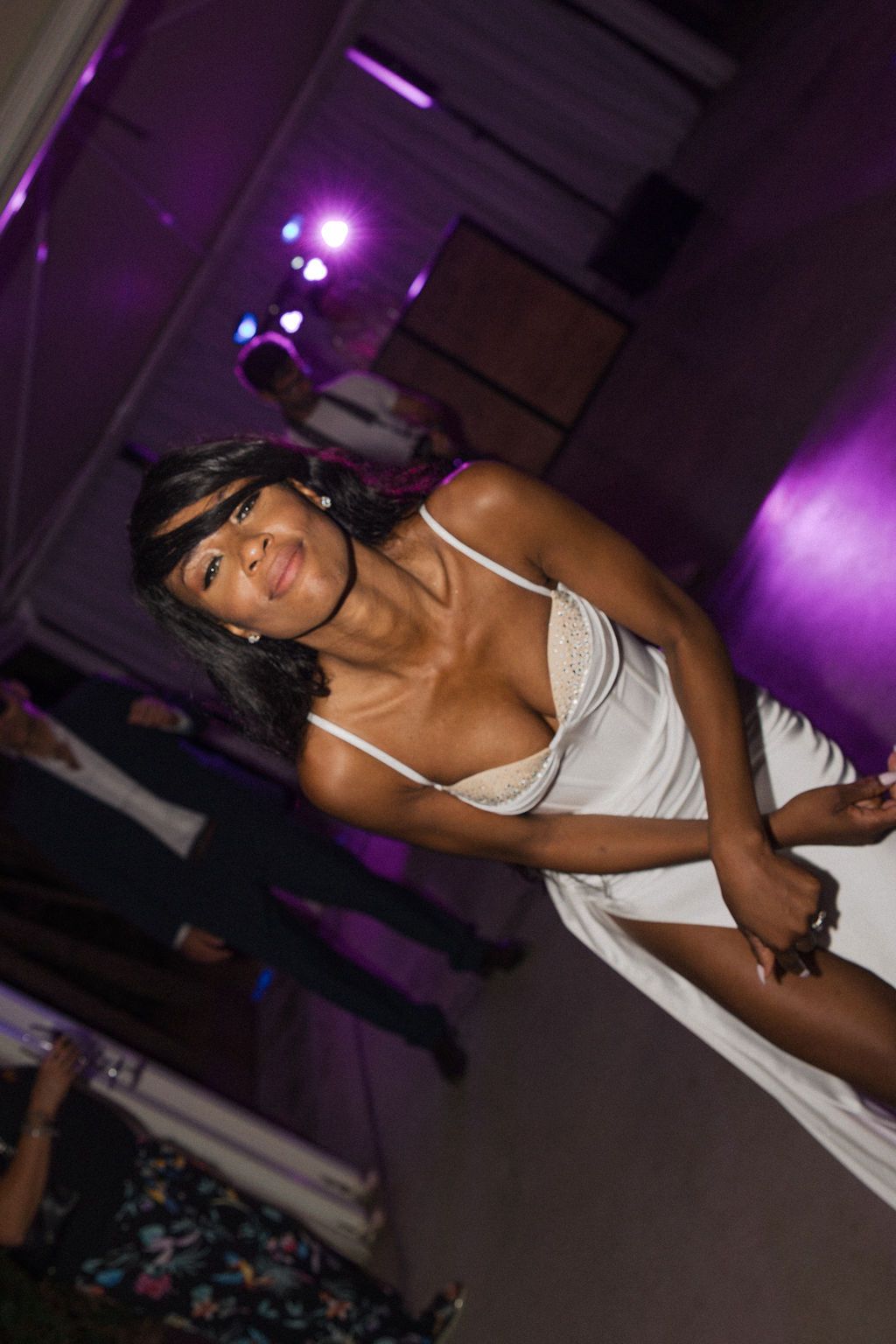 A dancer in white performs expressive moves under dramatic purple stage lighting.