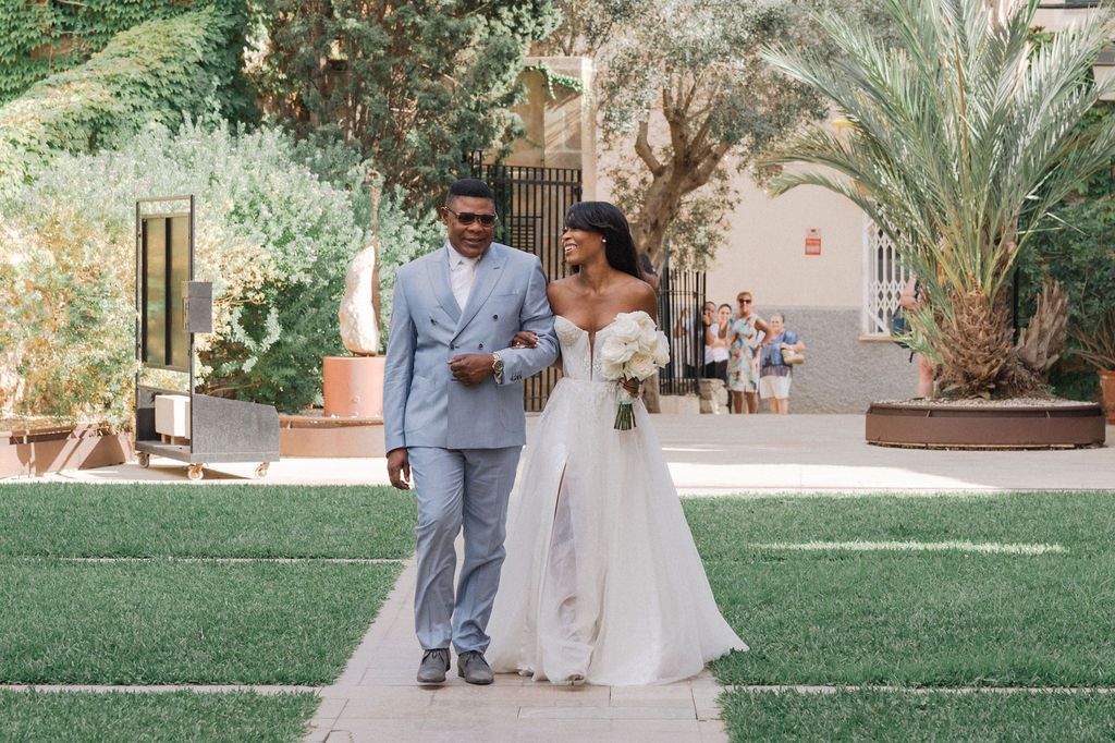 Outdoor wedding celebration in a lush garden setting with stone architecture in the background.