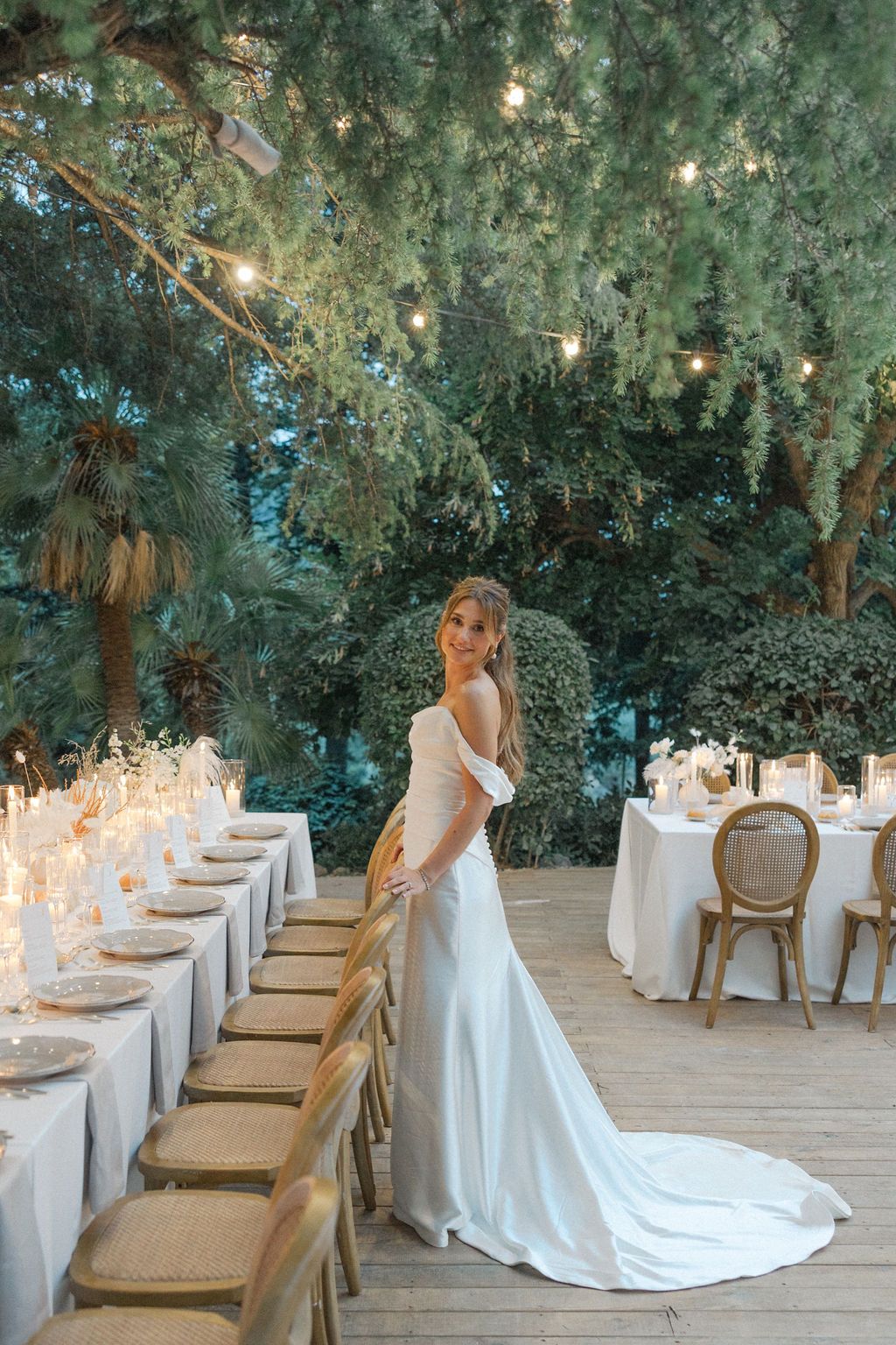 Elegant outdoor wedding reception setup with white table settings and string lights in a garden setting.