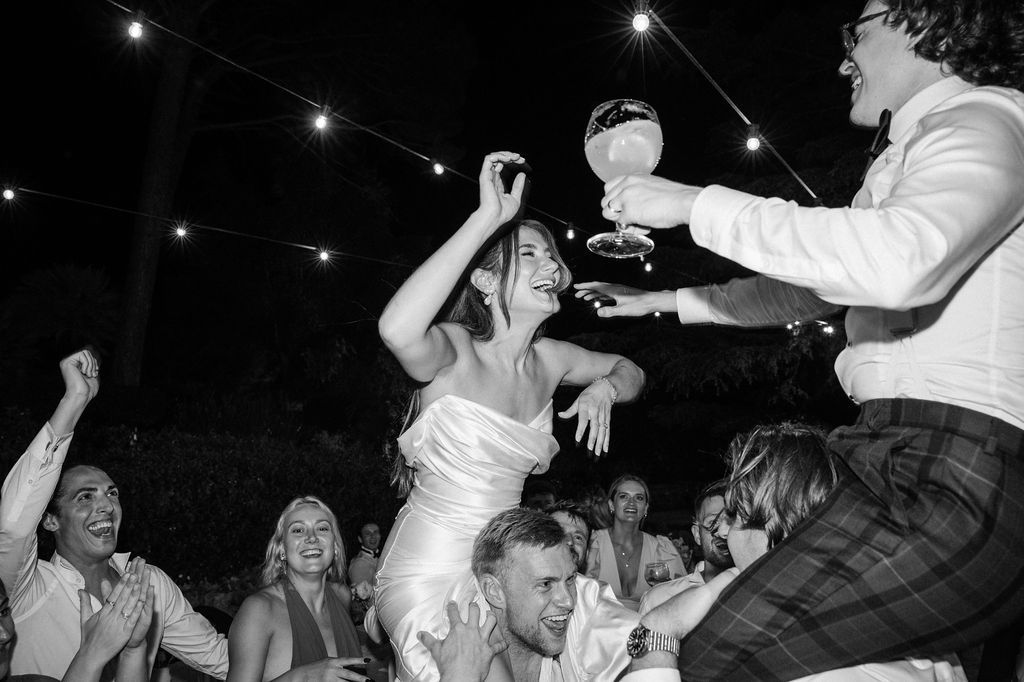 Wedding guests dance energetically on a dark dance floor during a reception celebration.