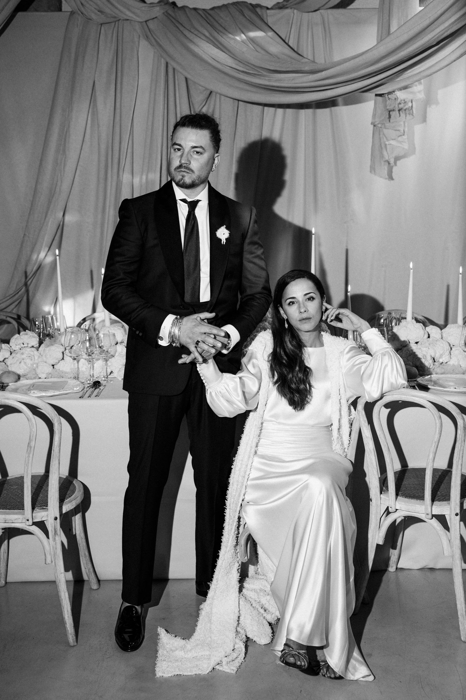 Wedding reception scene with couple in formal attire seated among elegant table settings.