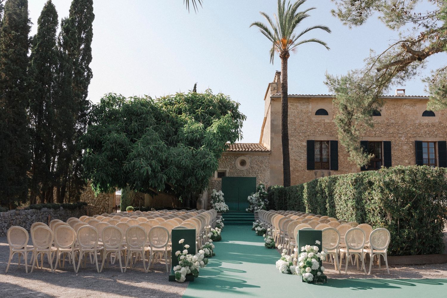 Elegant outdoor wedding venue with rows of chairs and greenery against a Mediterranean-style backdrop.