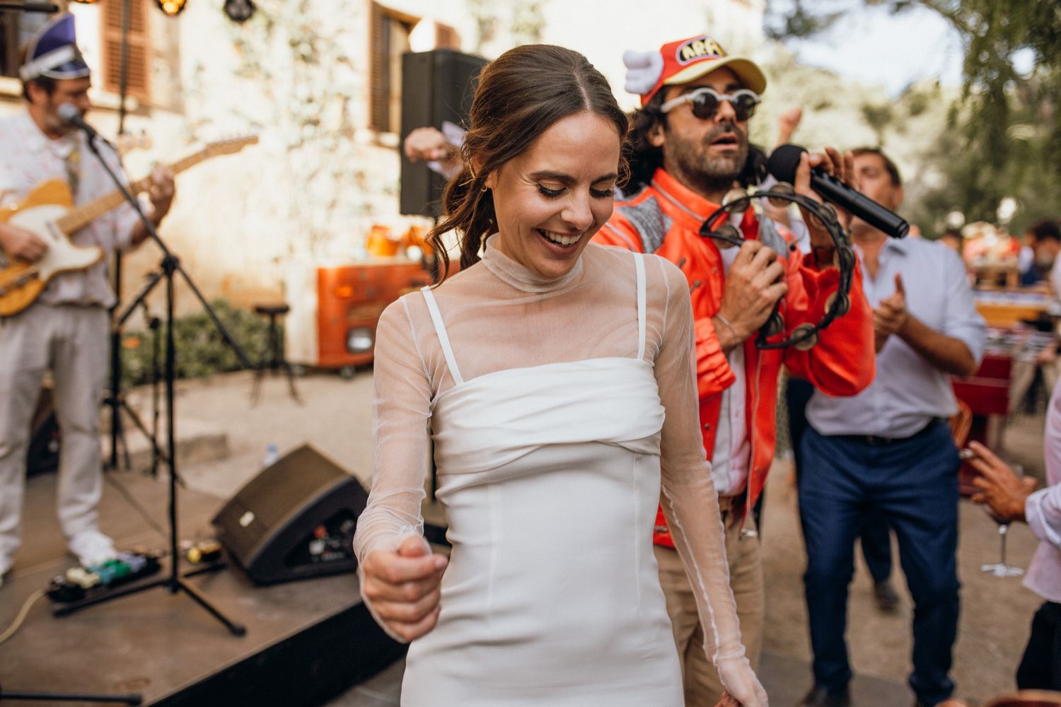 A bride in a white dress dances at an outdoor wedding reception while a band performs in the background.