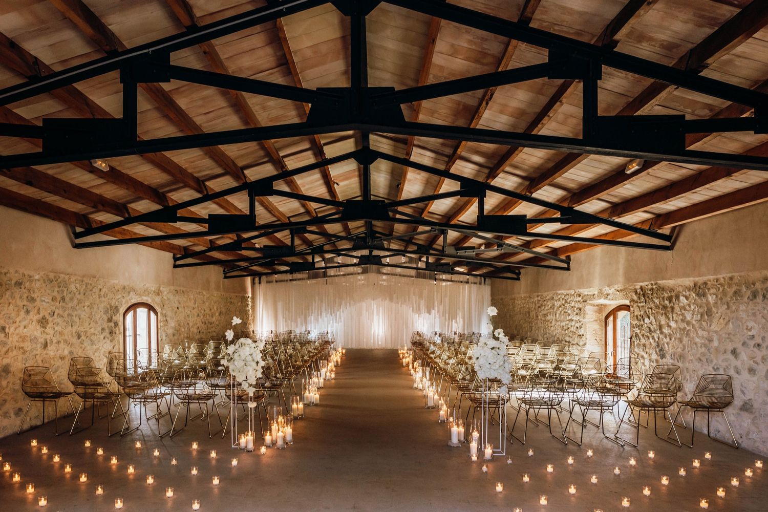 Rustic barn wedding venue with exposed wooden beams and romantic string lights illuminating the stone-walled reception space.
