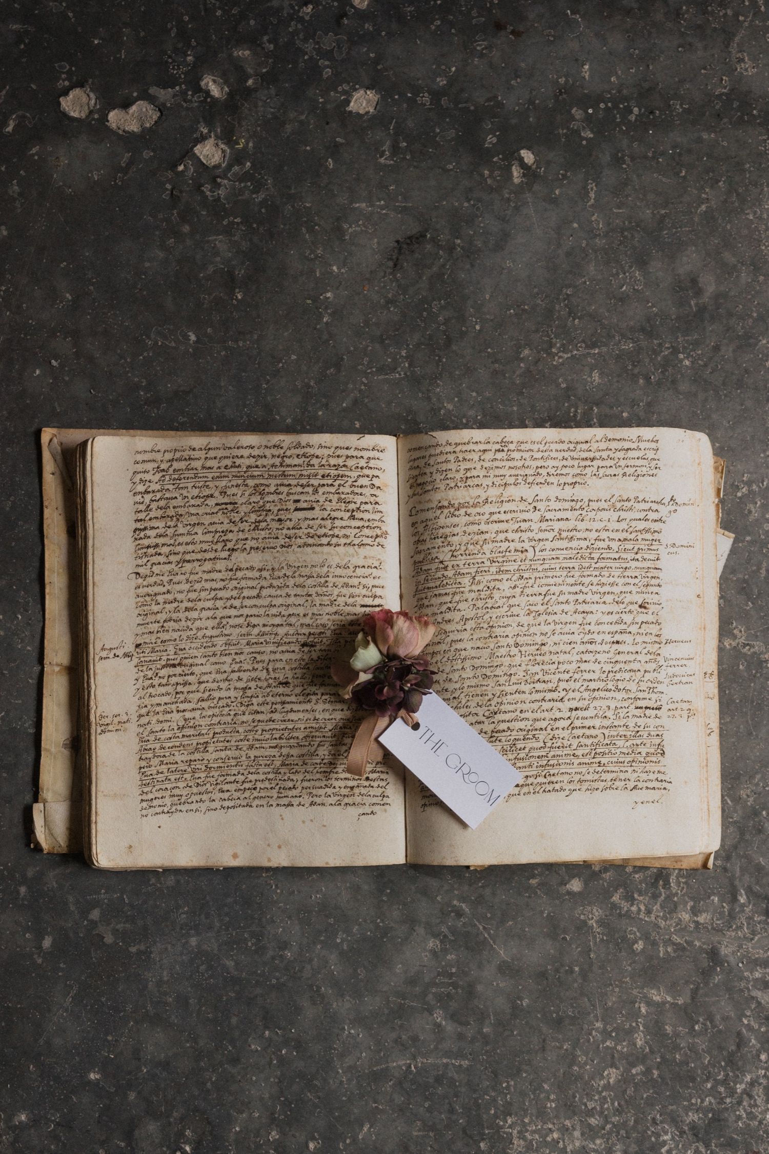 A vintage handwritten book lies open on a dark textured surface with a small tag attached to its pages.